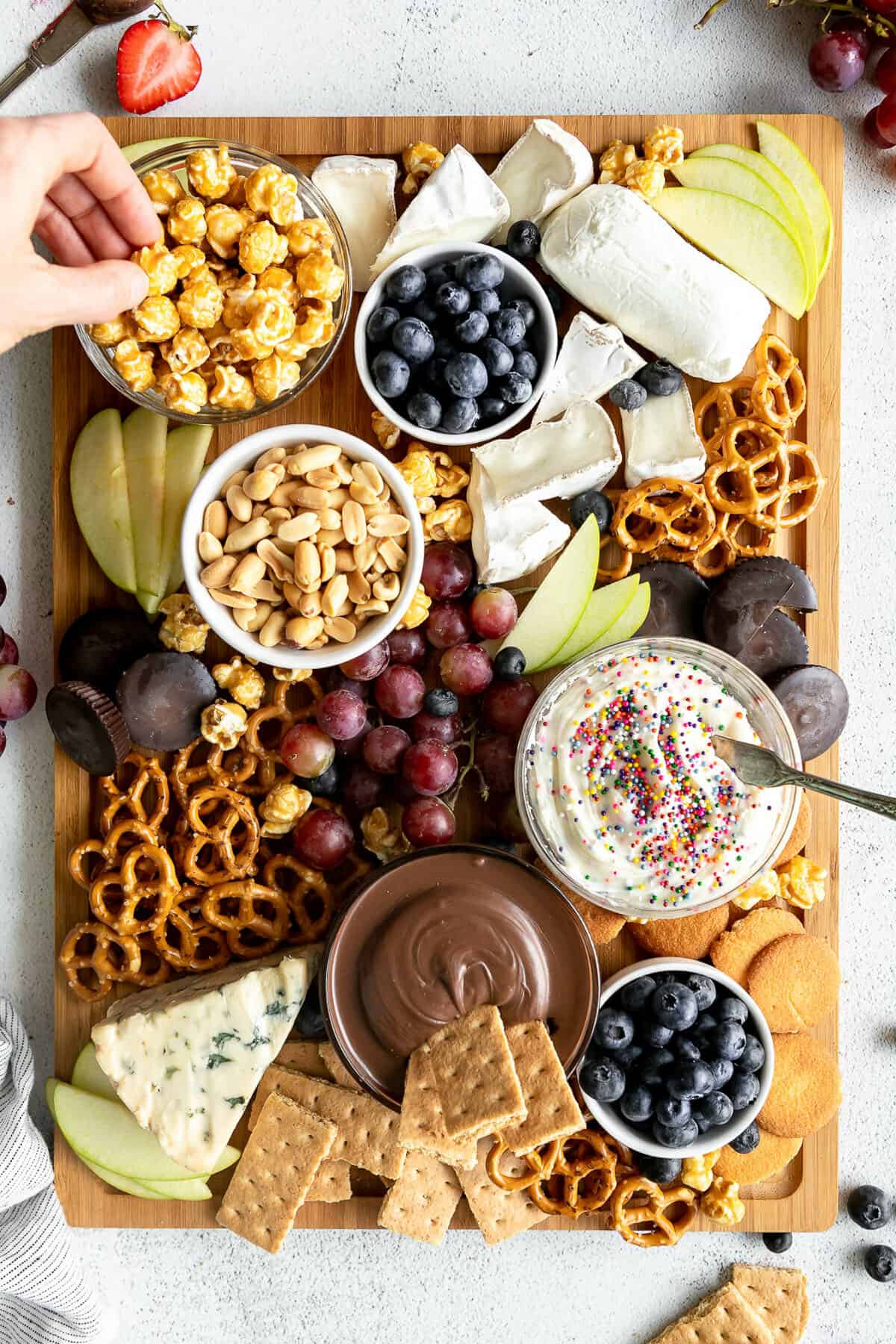 Large dessert charcuterie board filled with fruit, nuts, dips, and candy.