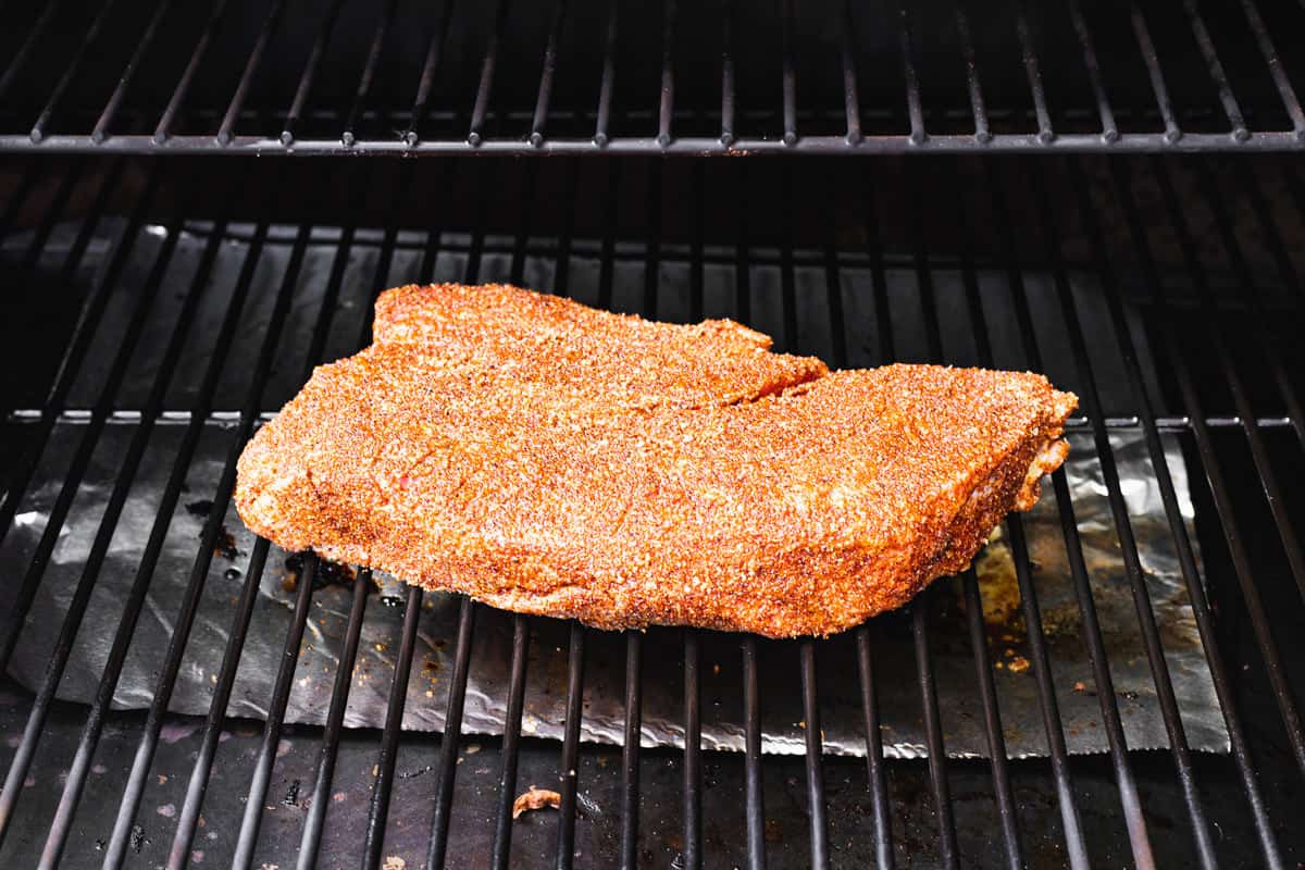 Seasoned chuck roast on the grill grates of a smoker.