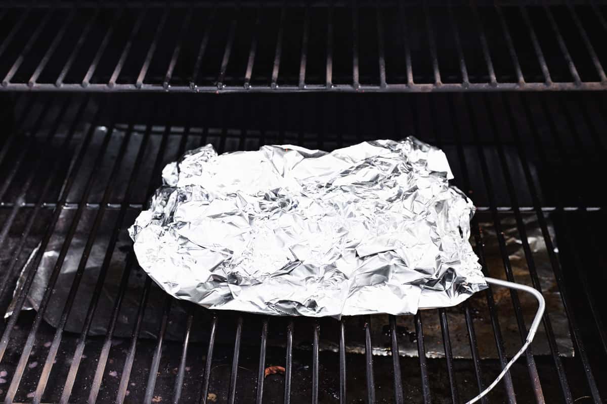 Foil-wrapped chuck roast on the grill grates of the smoker.