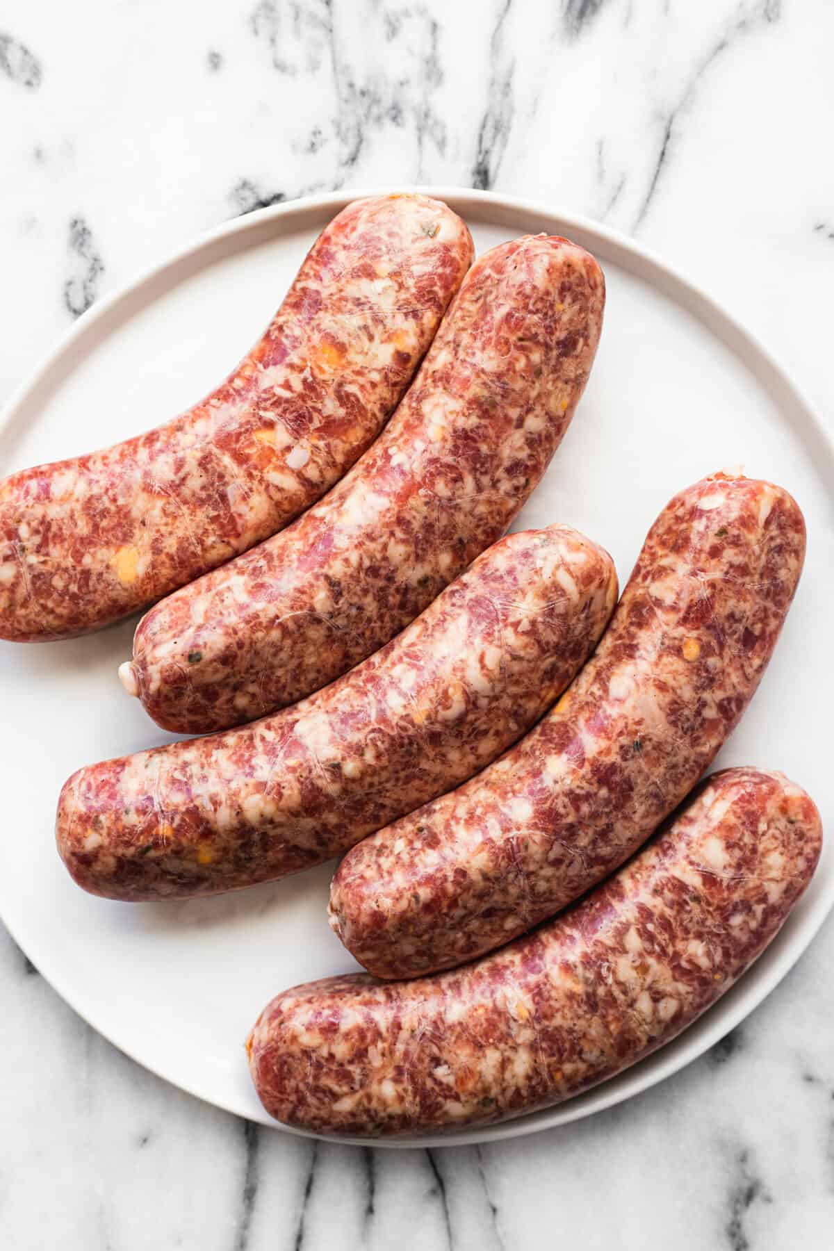 White plate with smoked cheddar jalapeno brats that are sliced.