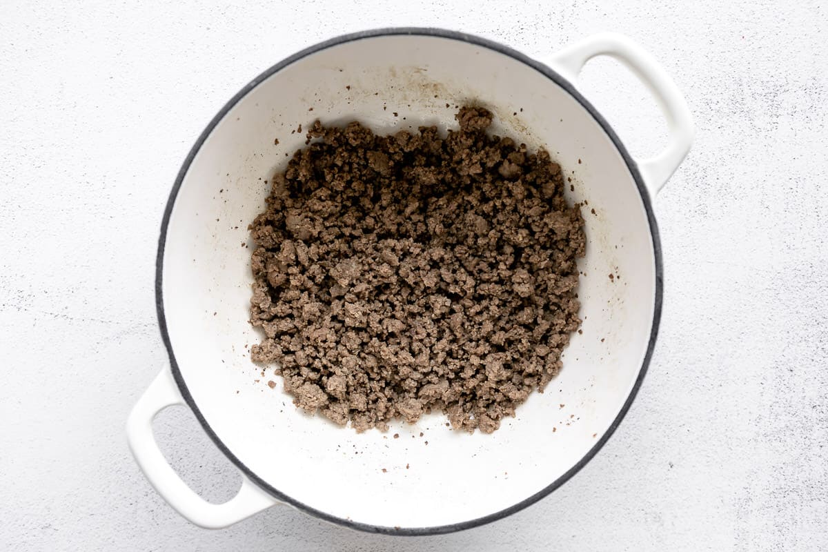 Browned ground beef in a large white pot.