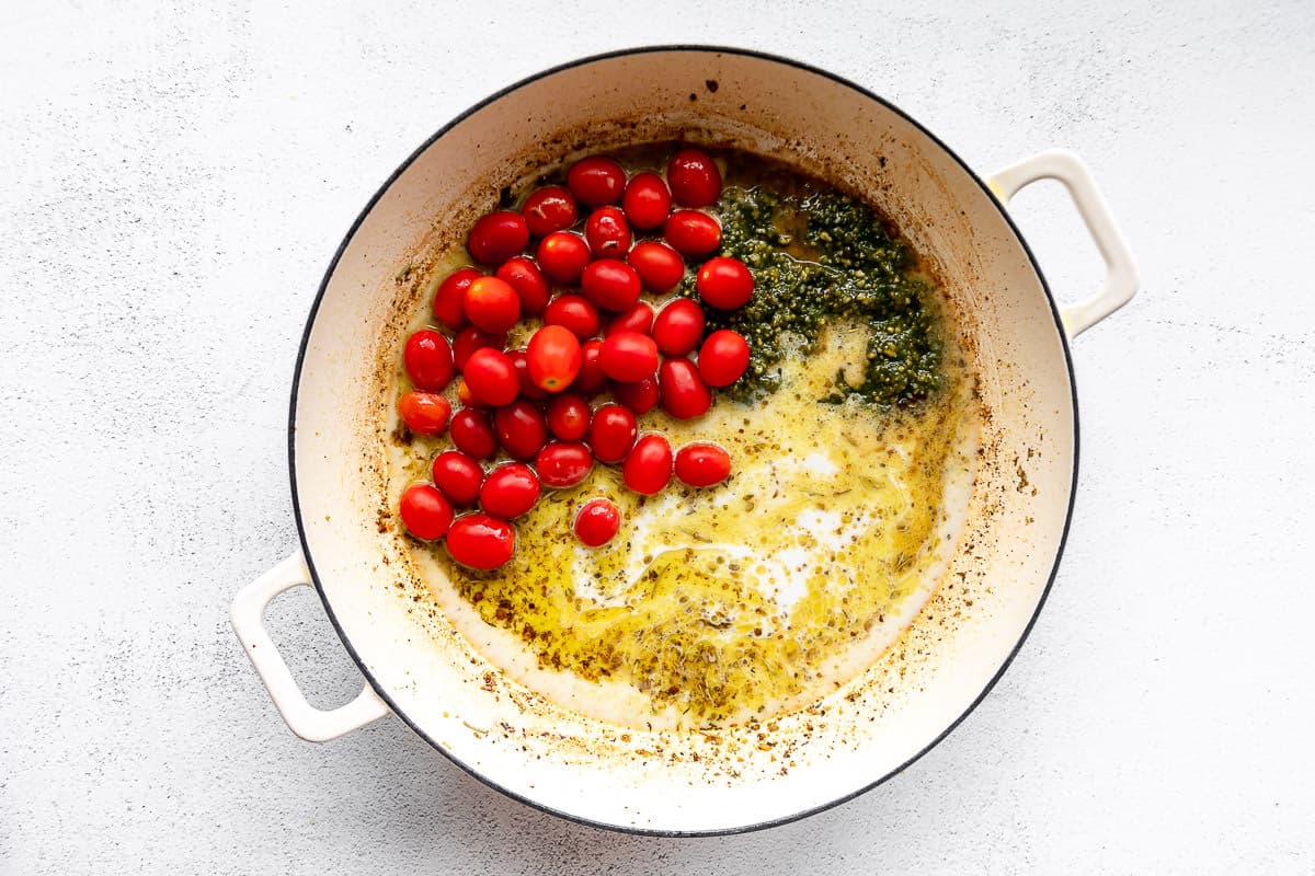 Large white pan with grape tomatoes, basil pesto, and heavy cream.