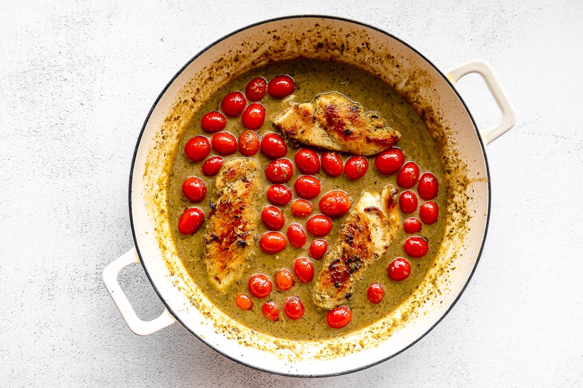 Large white pan filled with pesto chicken, creamy sauce, and grape tomatoes.
