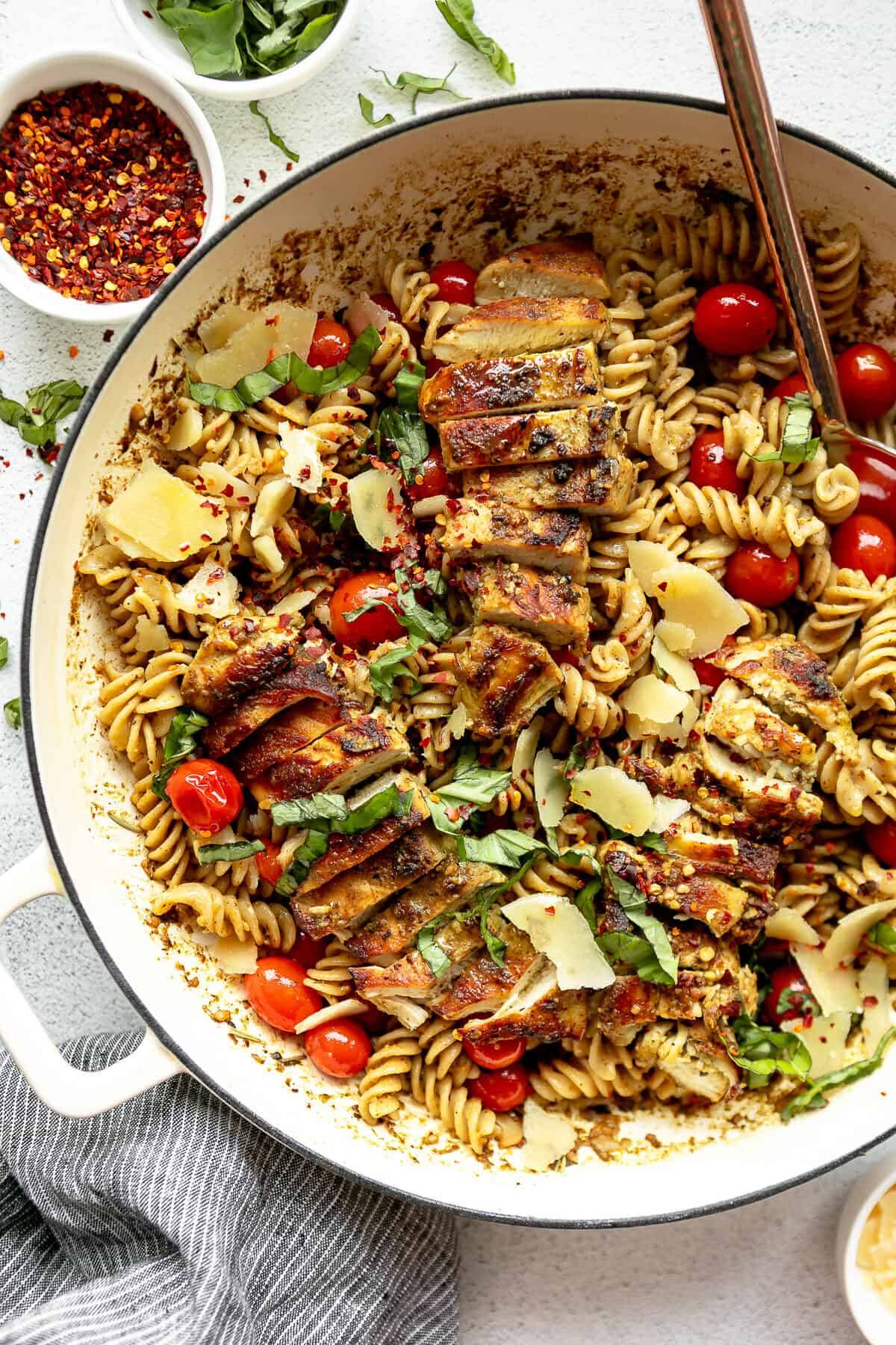 Large white pot filled with pesto pasta and grilled chicken garnished with basil.