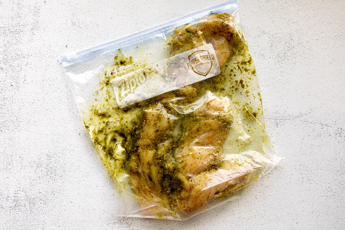 Ziploc bag filled with chicken breast marinating in pesto.