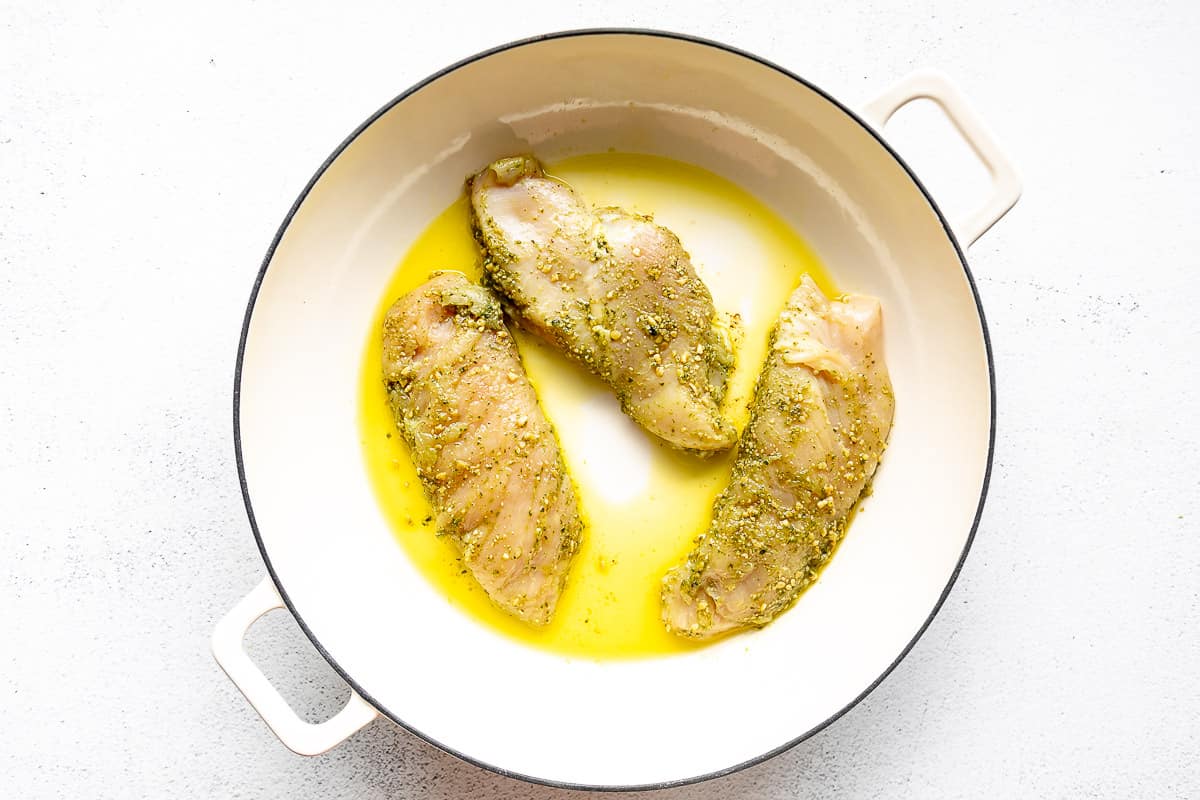 Large white pan with olive oil and pesto chicken.