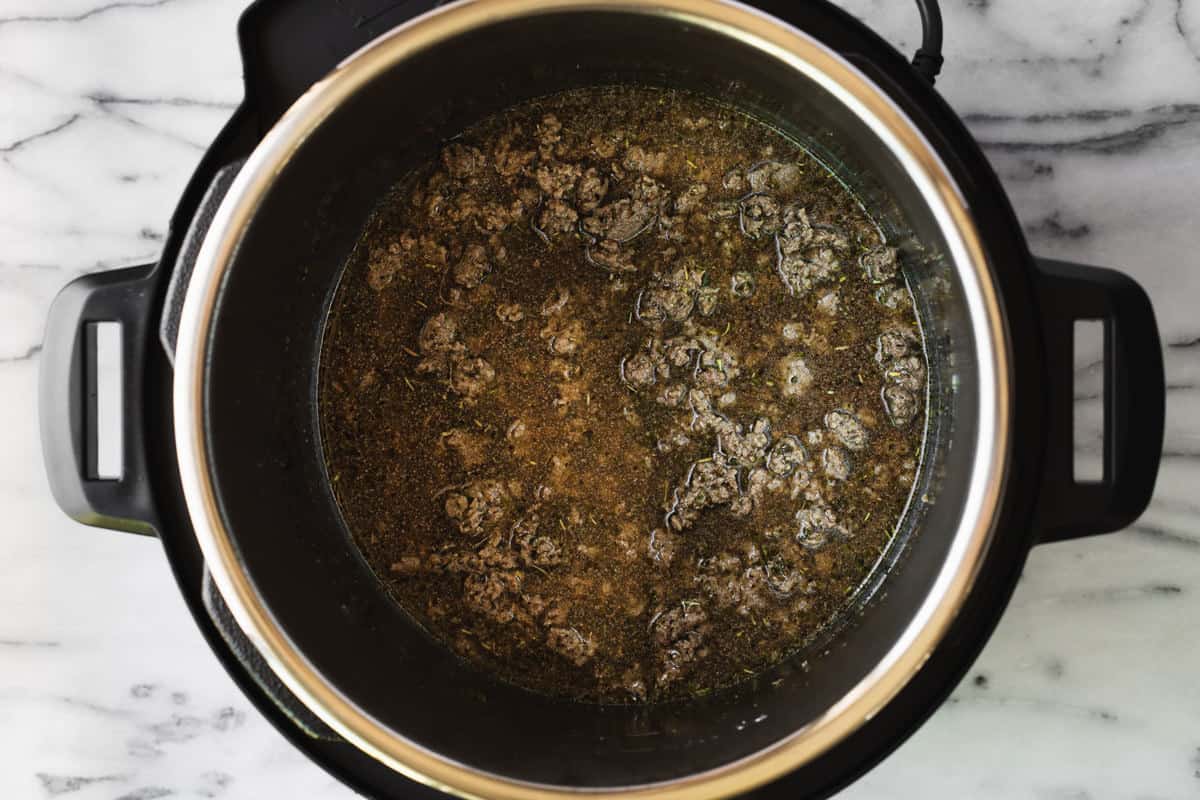 Instant pot filled with browned ground beef and broth.