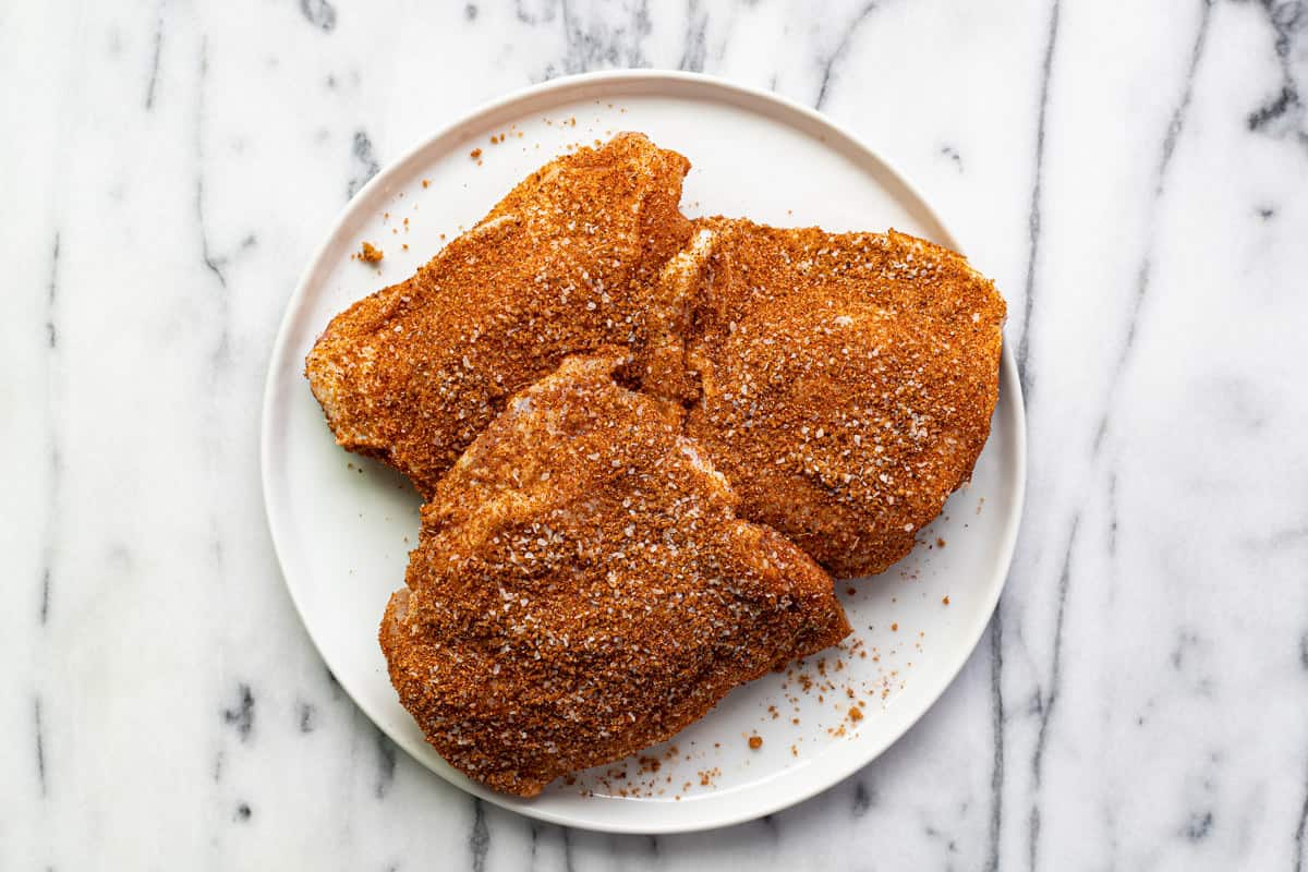 Chicken thighs that have been seasoned with dry rub on a white plate.