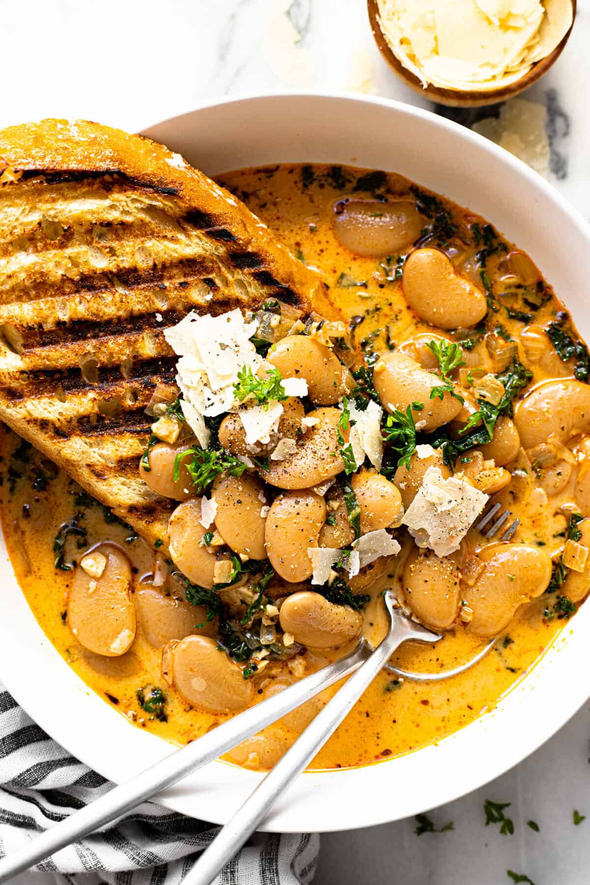 White bowl filled with brothy lima beans, Parmesan cheese, and toasted sourdough bread.