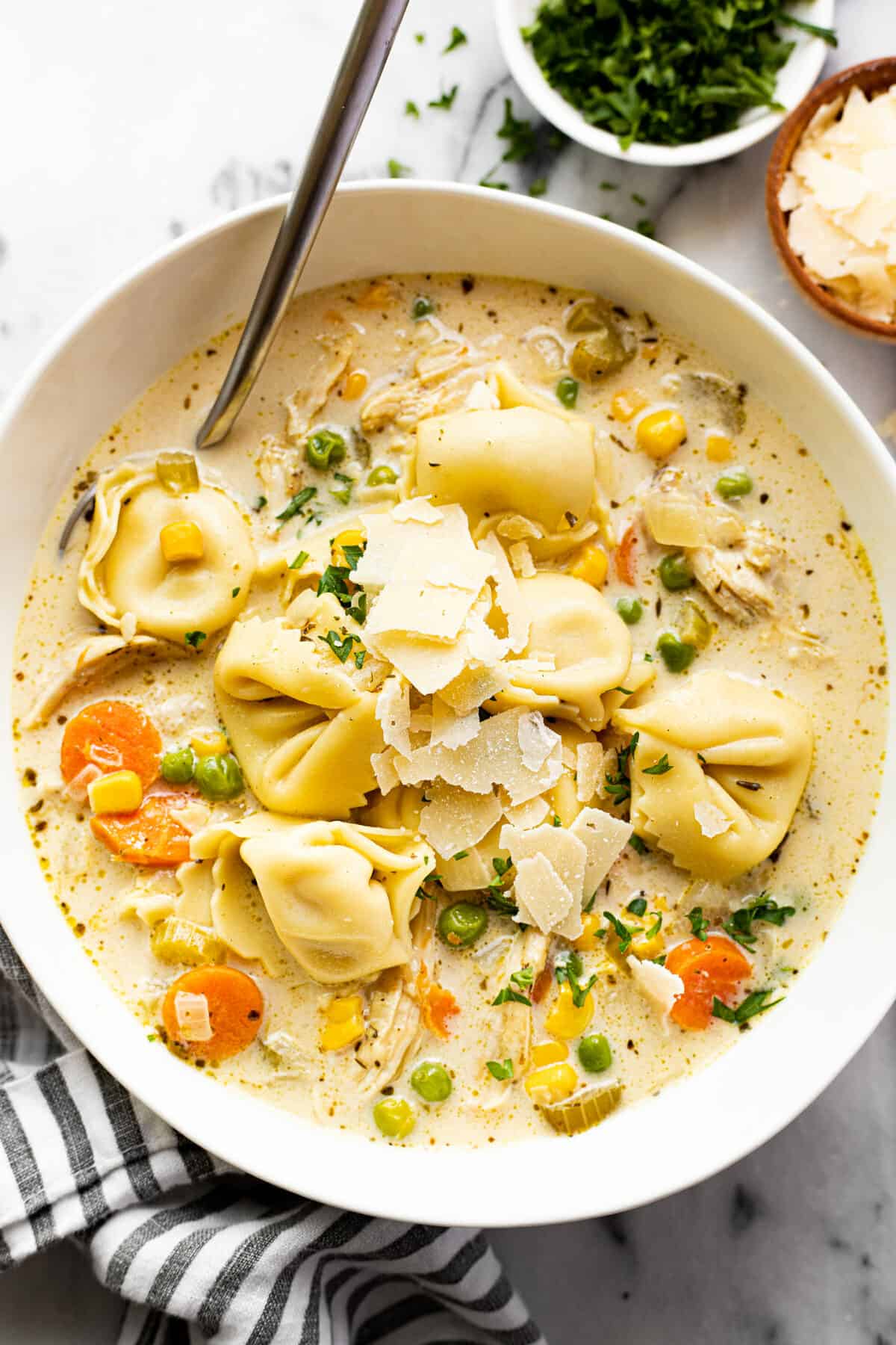 White bowl filled with homemade chicken tortellini soup garnished with Parmesan cheese.