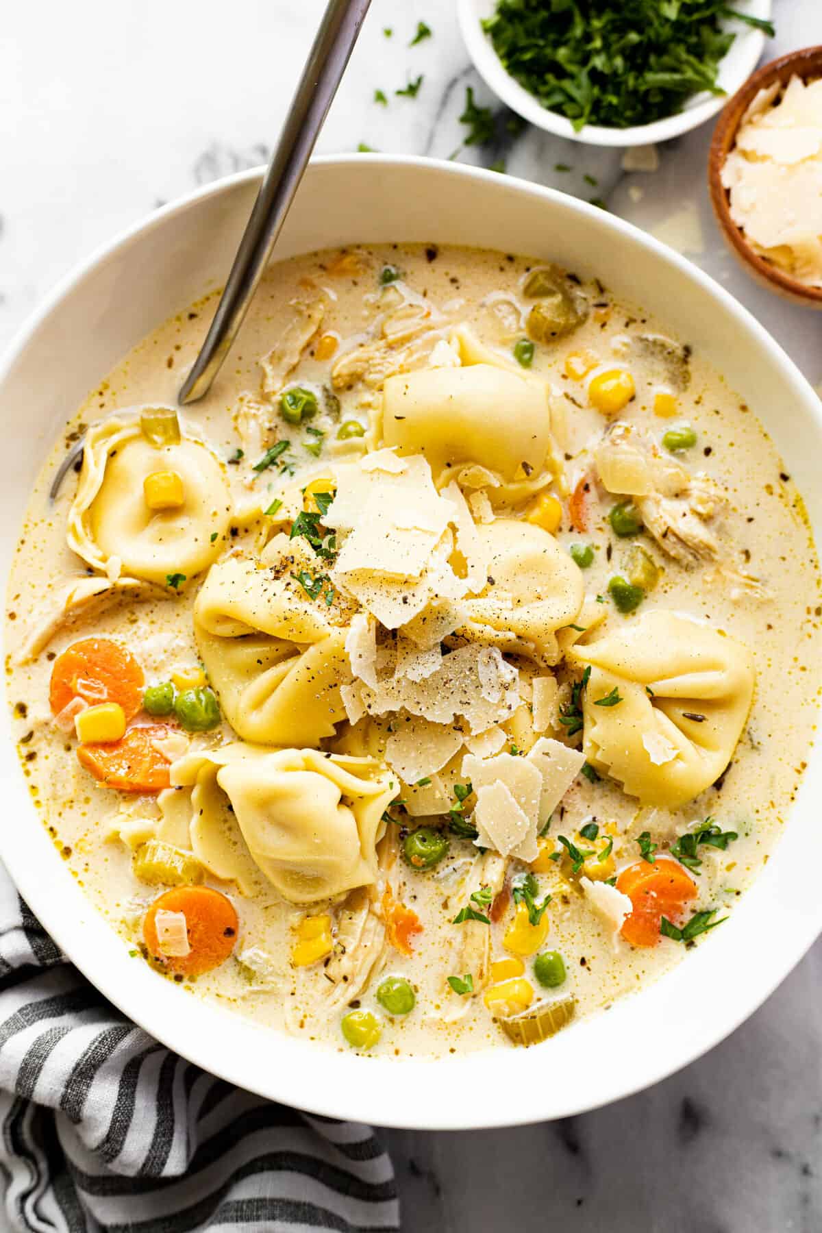 White bowl filled with homemade chicken tortellini soup garnished with Parmesan cheese.