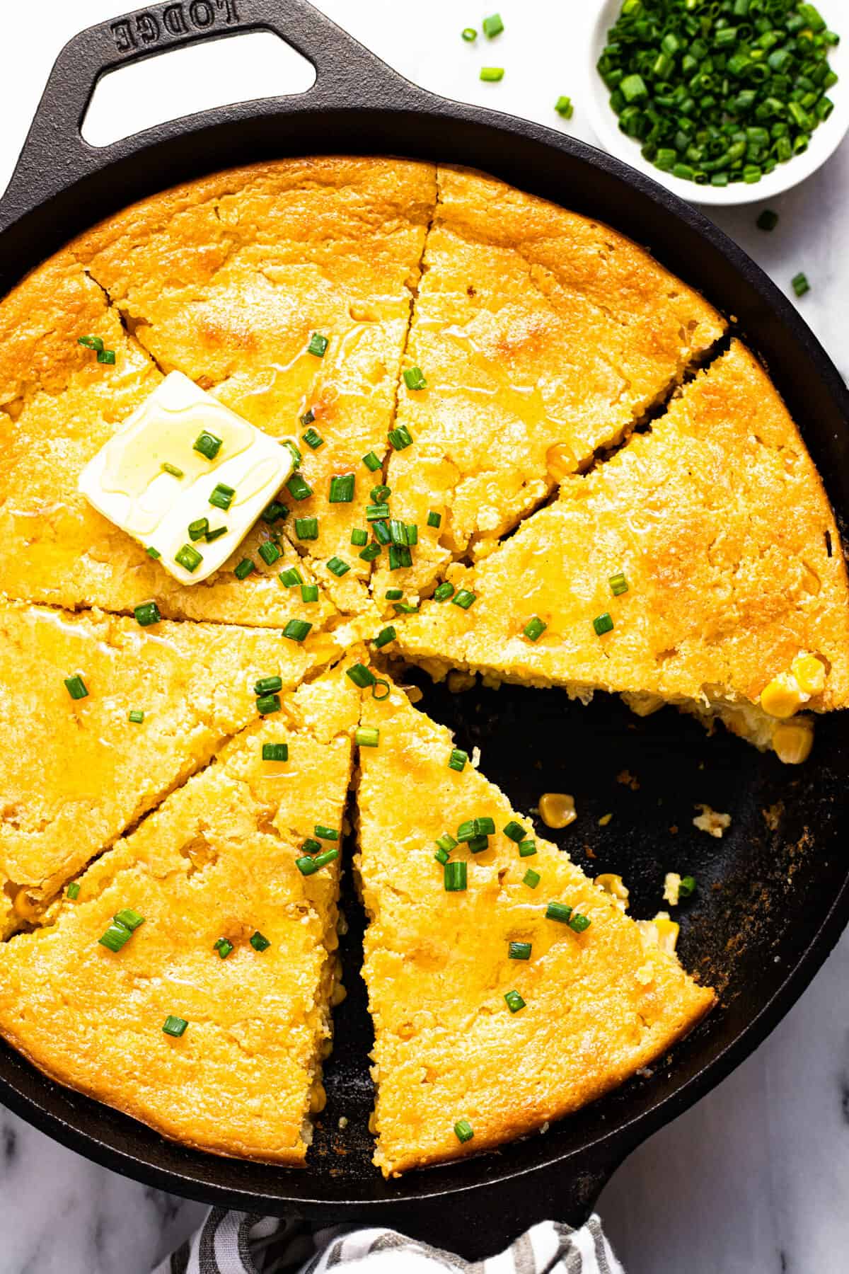Sliced cornbread casserole topped with chives and butter and drizzled with honey. 