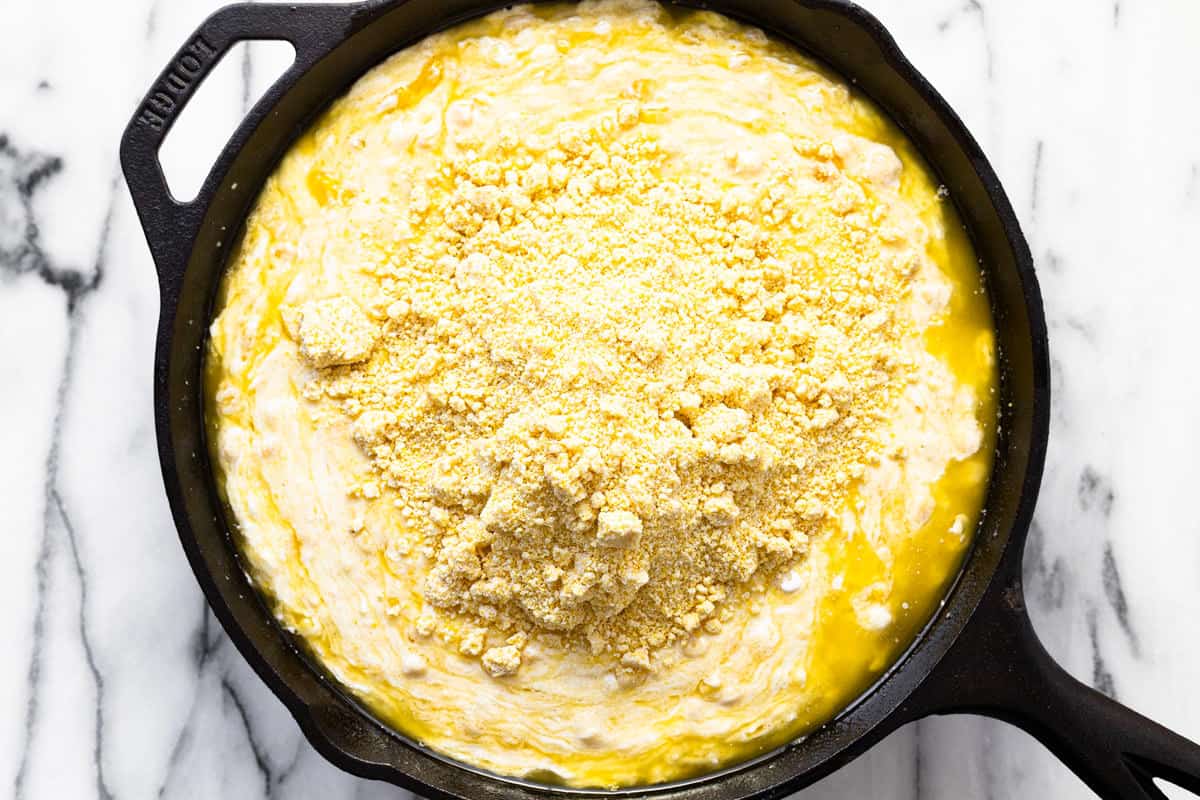 Large cast iron pan filled with ingredients to make homemade cornbread casserole.