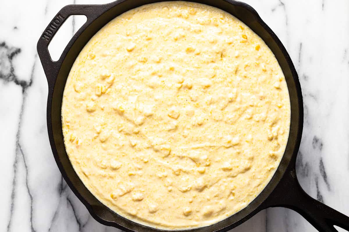 Large cast iron pan filled with ingredients to make homemade cornbread casserole.