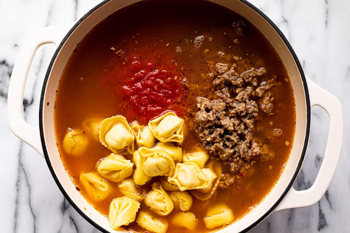 Large white pot filled with ingredients to make sausage tortellini soup.