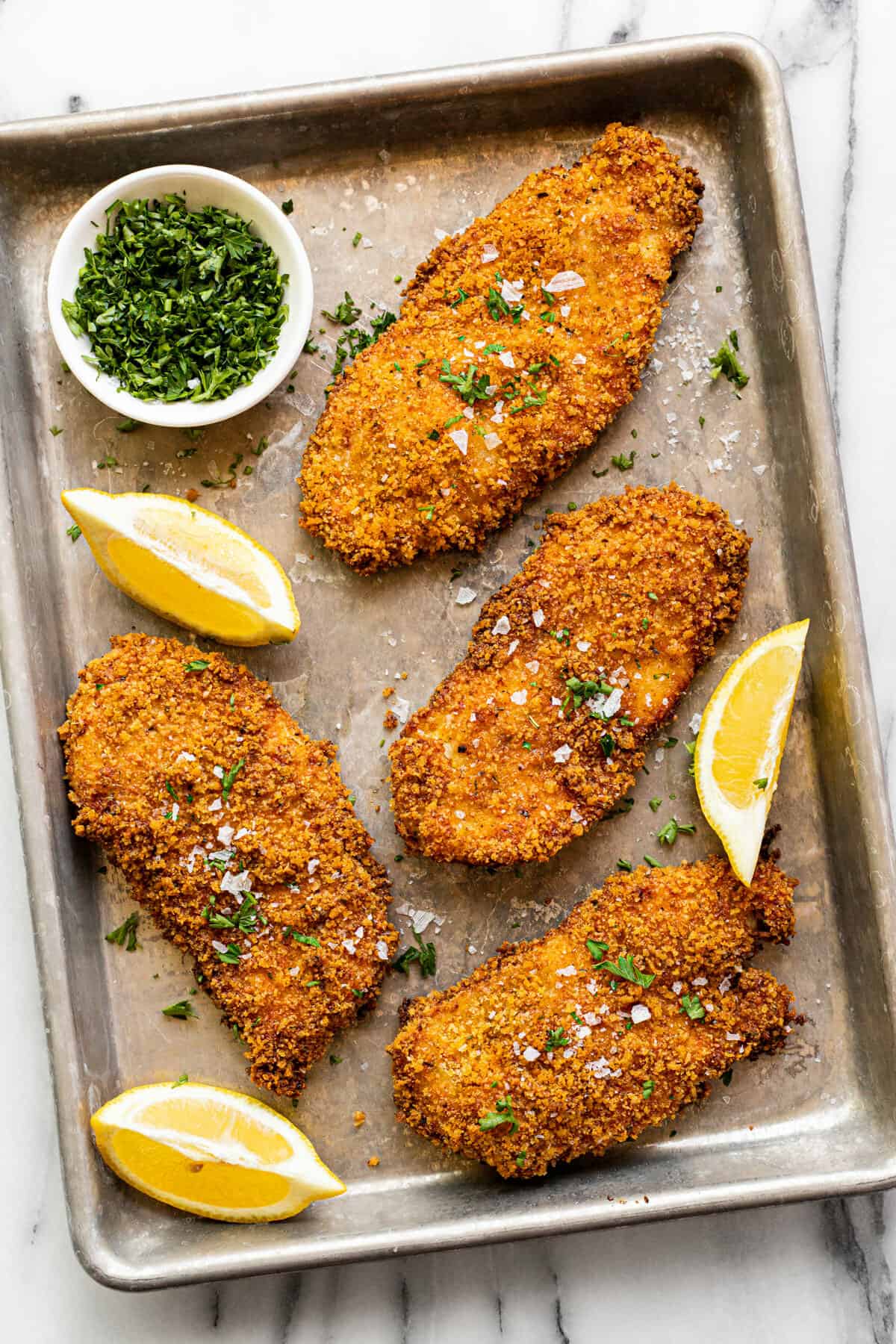 Metal sheet pan with Panko crusted chicken garnished with fresh parsley. 