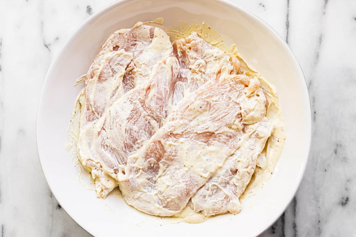 Marinated chicken in a mayonnaise mustard mixture in a white bowl.