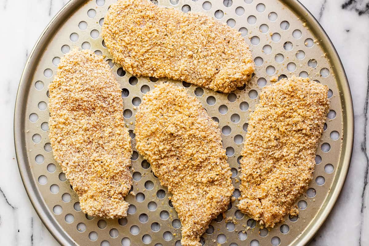 Panko crusted chicken breasts on a pizza pan.