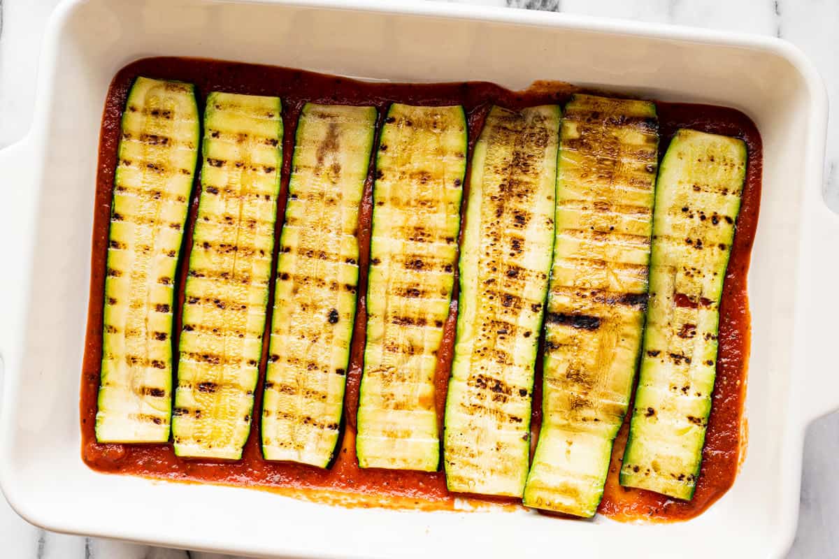 Red sauce and grilled zucchini in a large white baking dish.