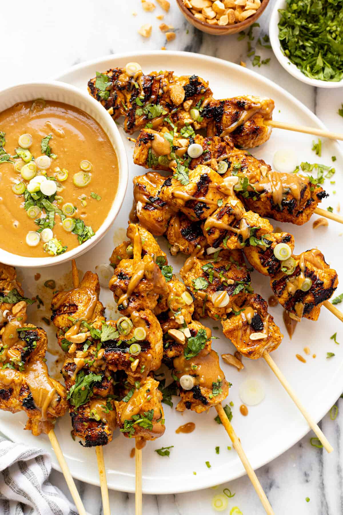 White plate with homemade chicken skewers and a bowl of peanut sauce.