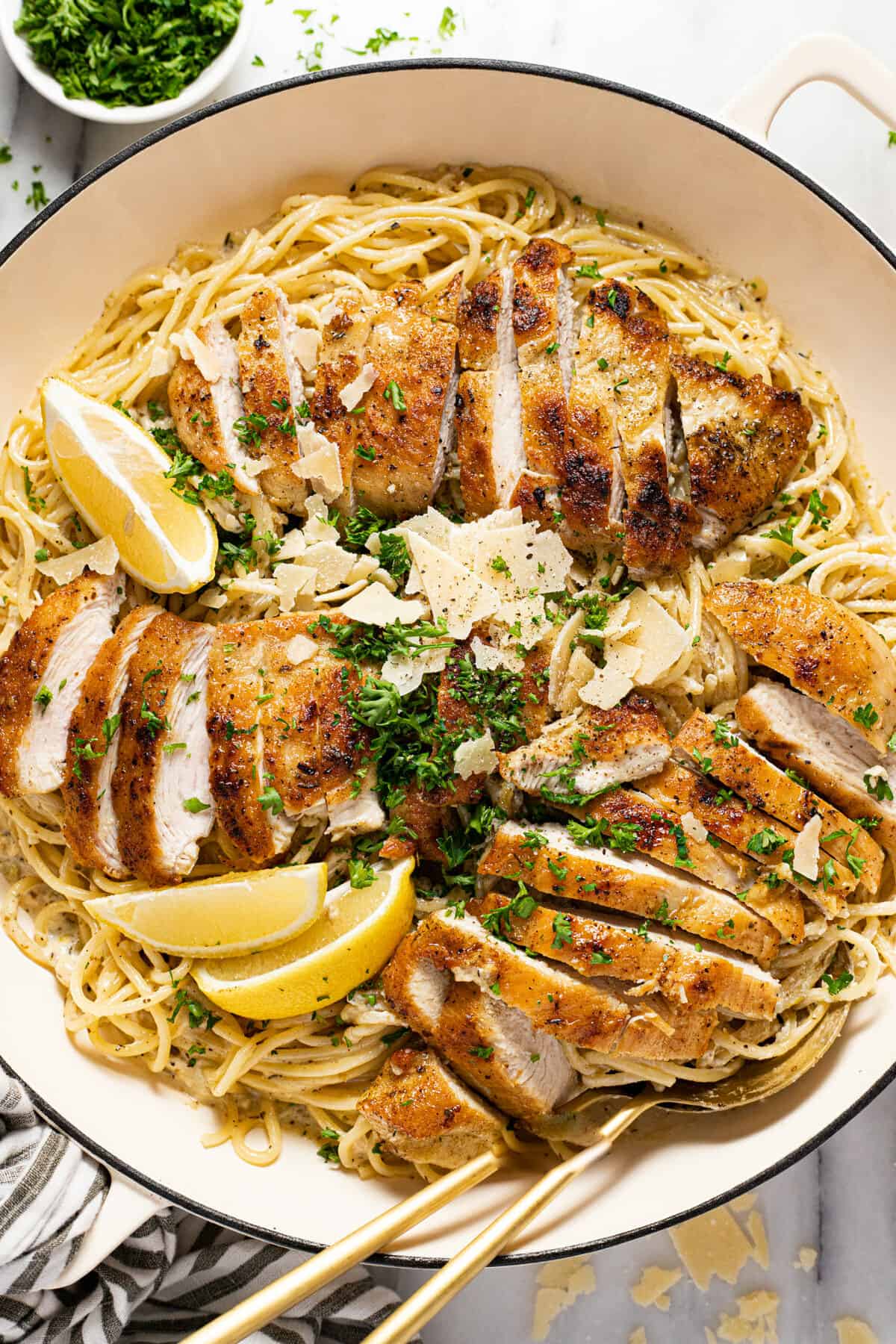 Large white pan filled with creamy spaghetti and sliced lemon chicken garnished with parsley.