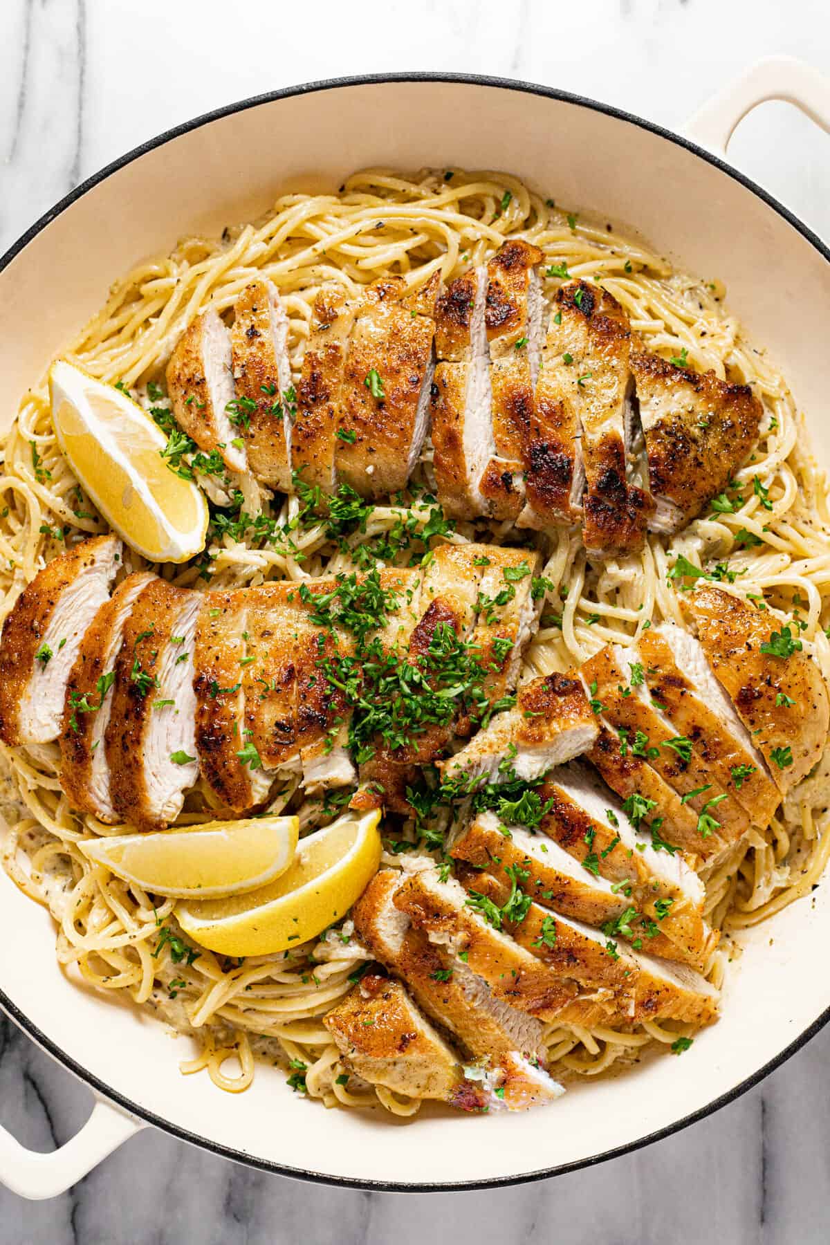 Large white pan filled with creamy spaghetti and sliced lemon chicken garnished with parsley.