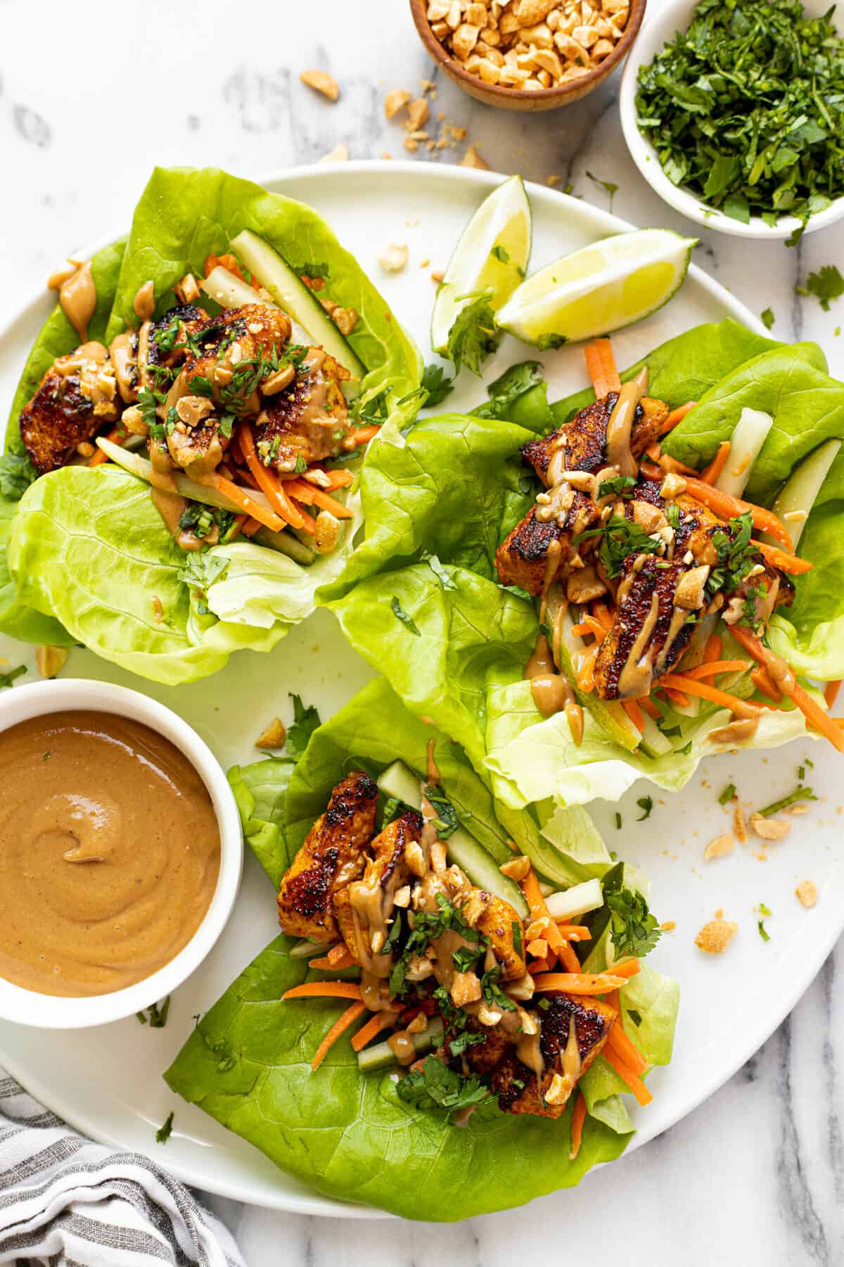 White plate with three chicken lettuce wraps and a bowl of peanut sauce.