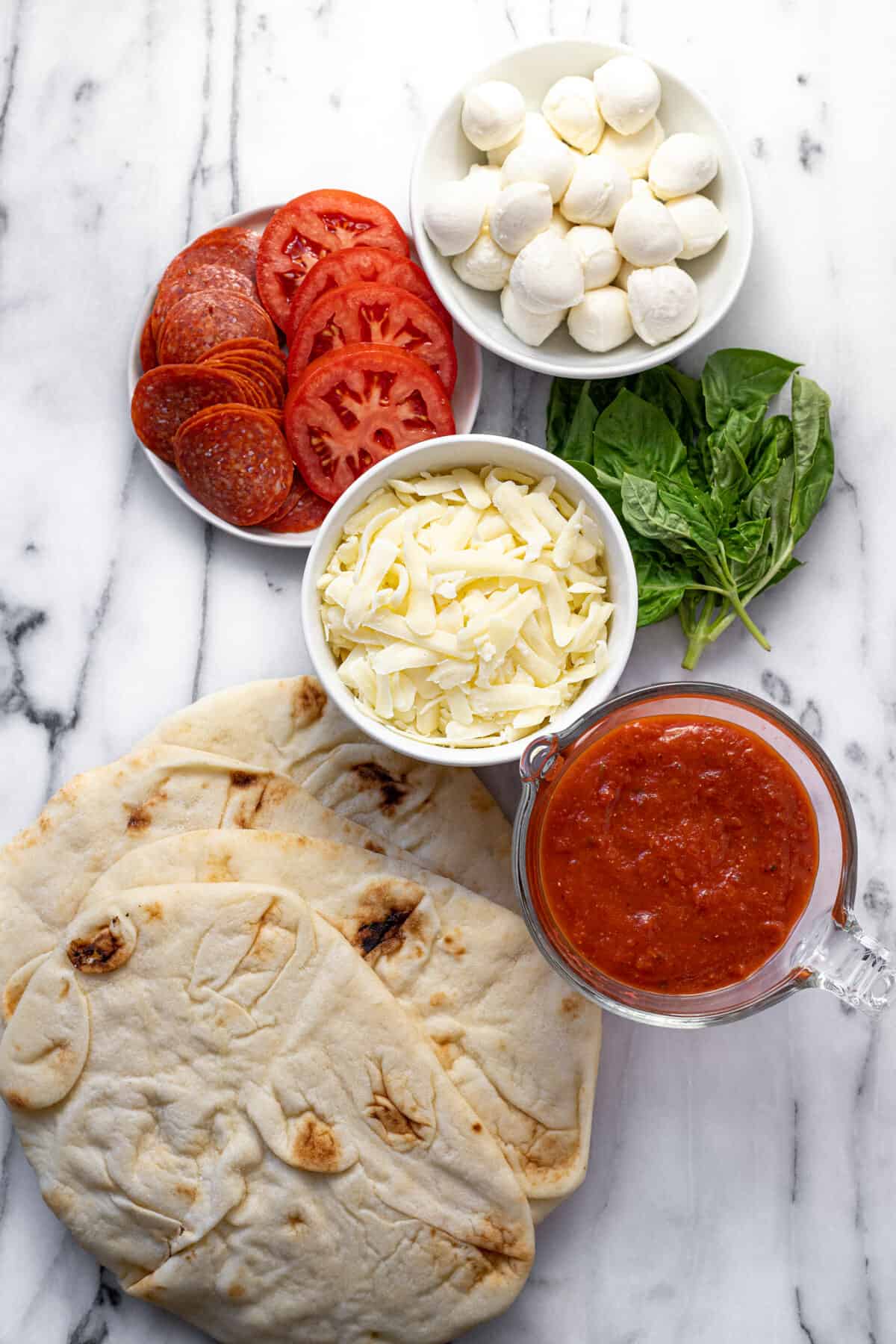 White marble counter top with ingredients to make naan pizza.