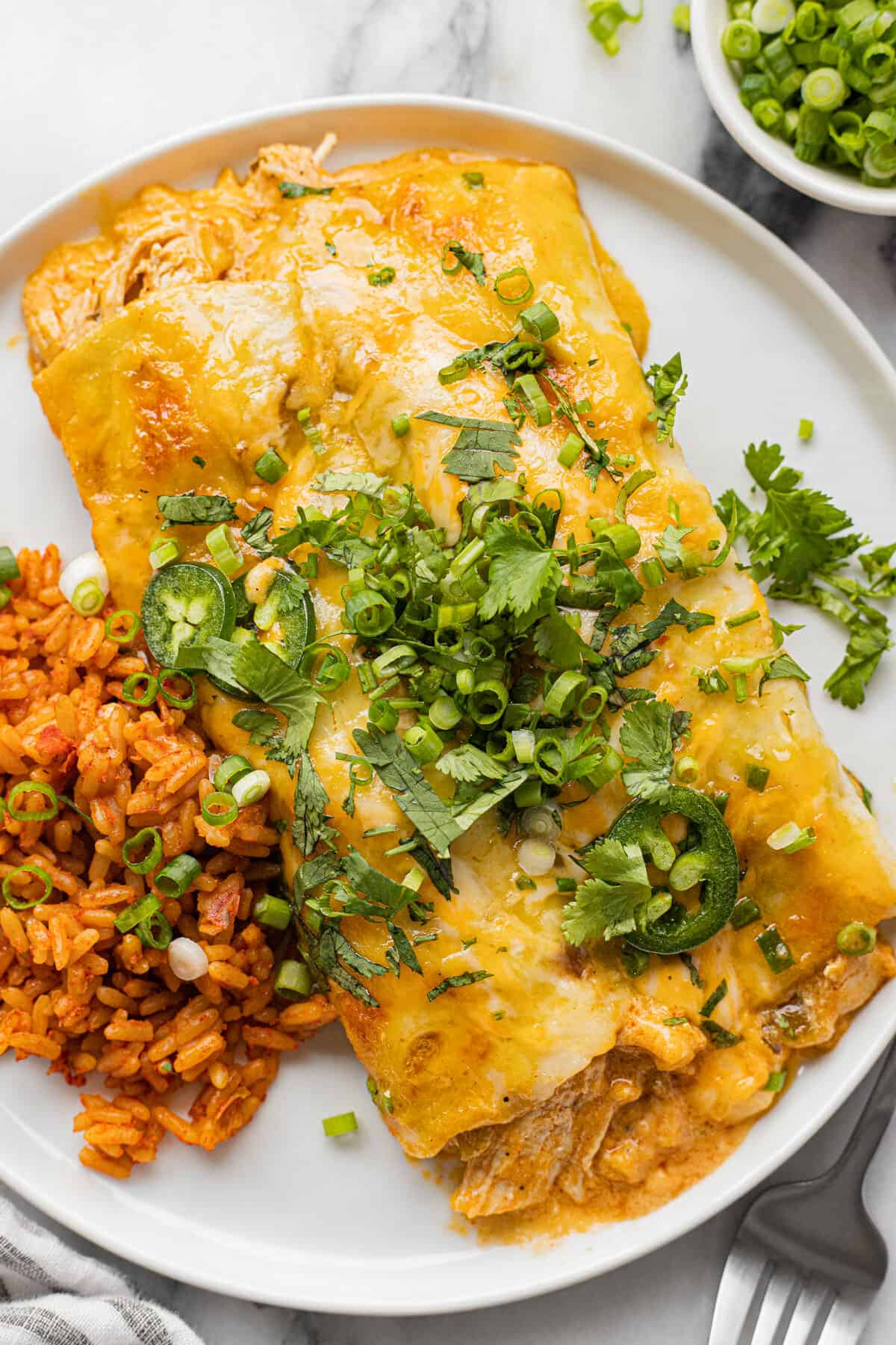 Two green enchiladas garnished with cilantro on a plate with rice.