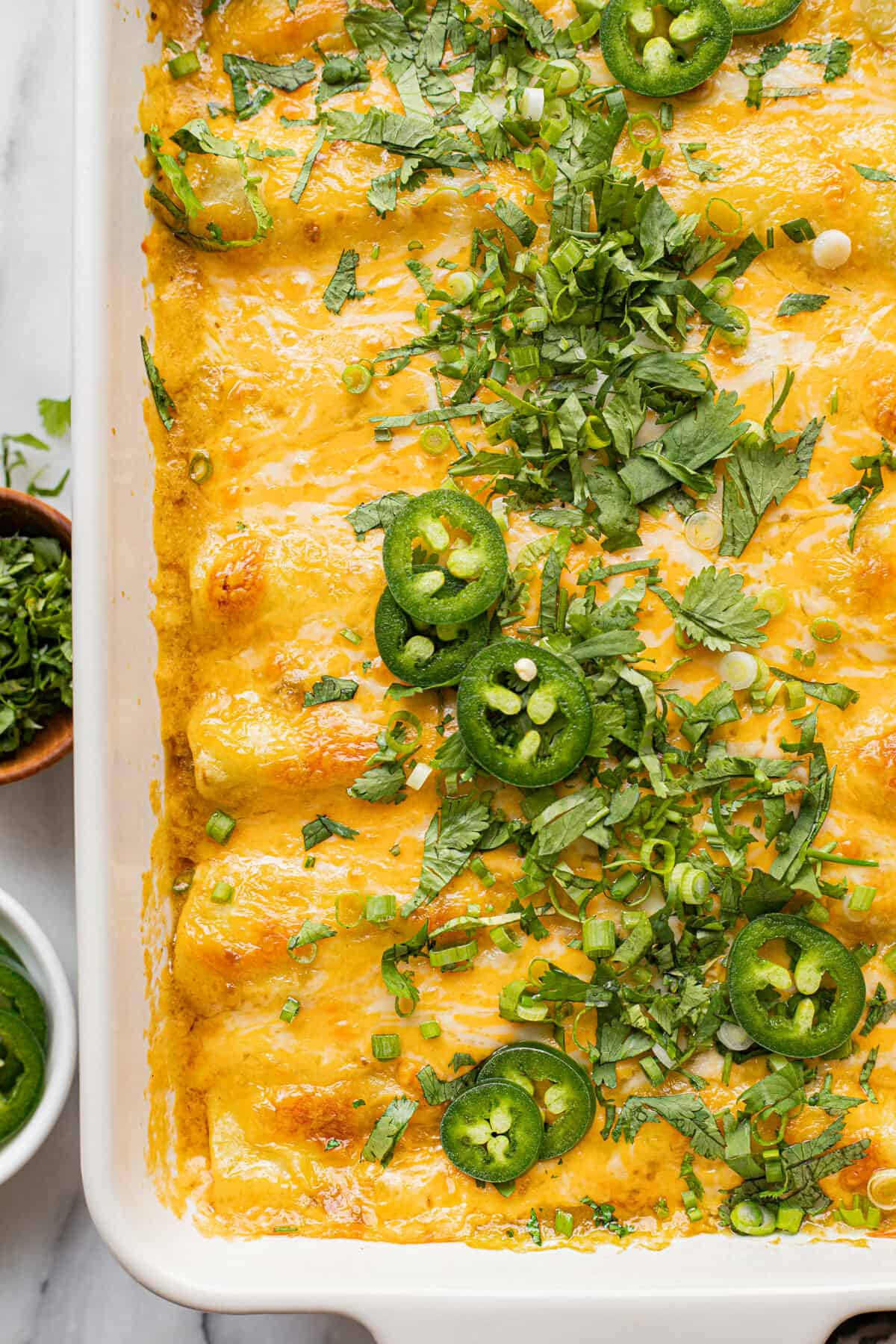 White baking dish filled with homemade chicken enchiladas garnished with cilantro.