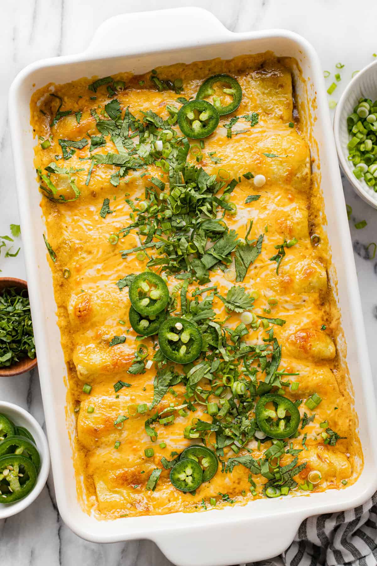 White baking dish filled with homemade chicken enchiladas garnished with cilantro.