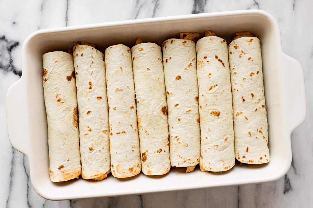 White baking dish filled with rolled enchiladas.