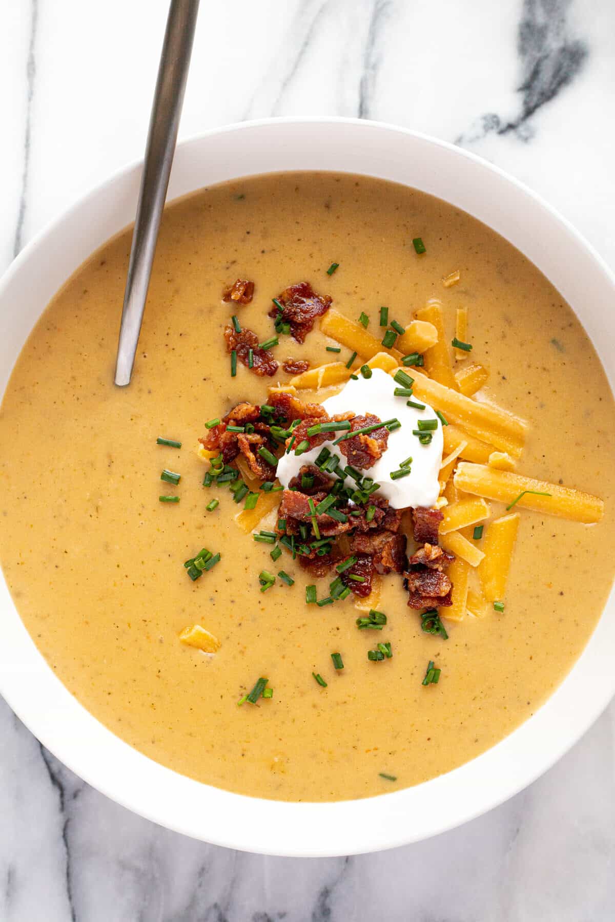 White bowl filled with creamy potato soup topped with cheddar and bacon.