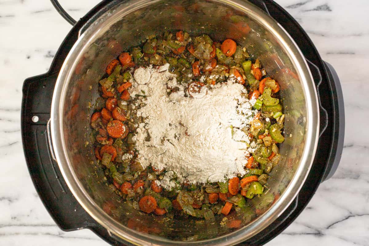 Flour sprinkled over sauteed veggies and herbs in an instant pot.