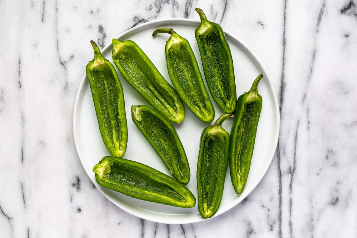 Halved jalapenos on a white plate.