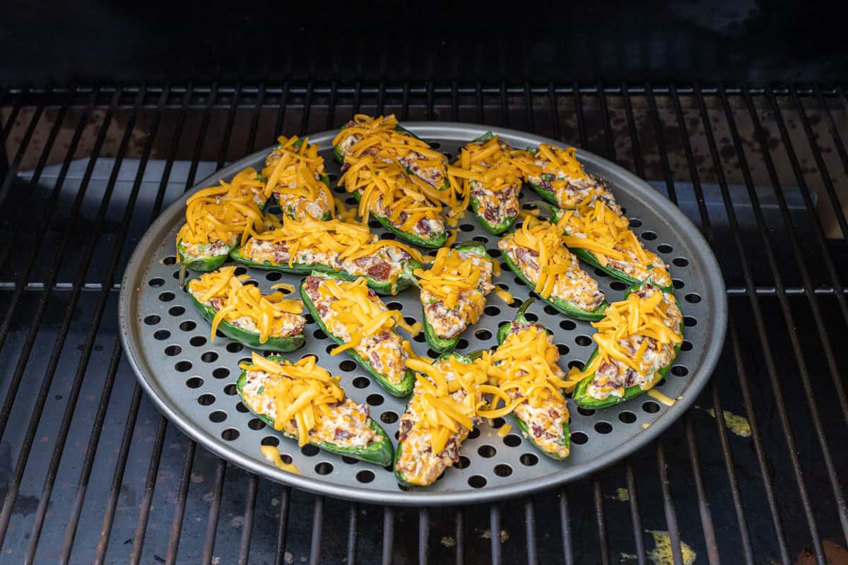 Jalapeno poppers on a pizza pan on a grill grate in the smoker.