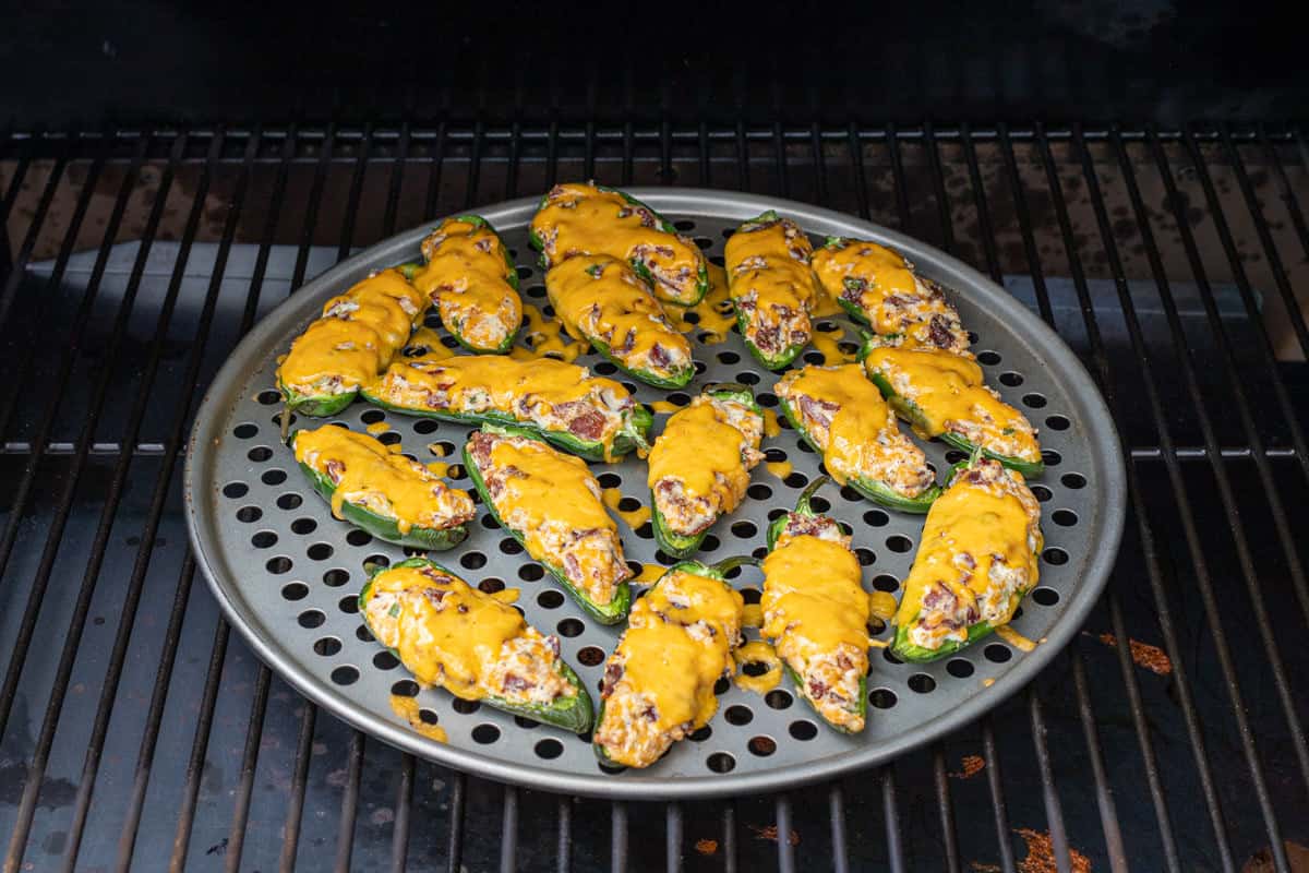 Freshly smoked jalapeno poppers on a pizza pan on a grill grate on a smoker.