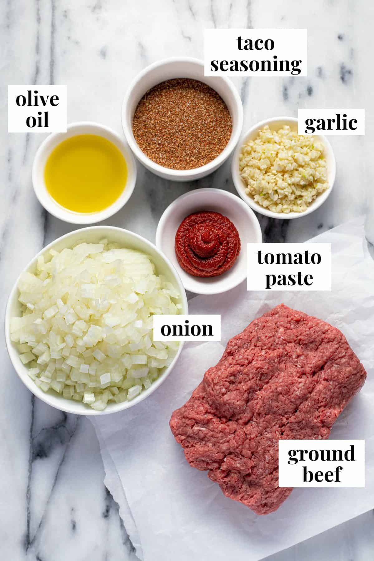White counter top with bowls of ingredients to make homemade taco meat.
