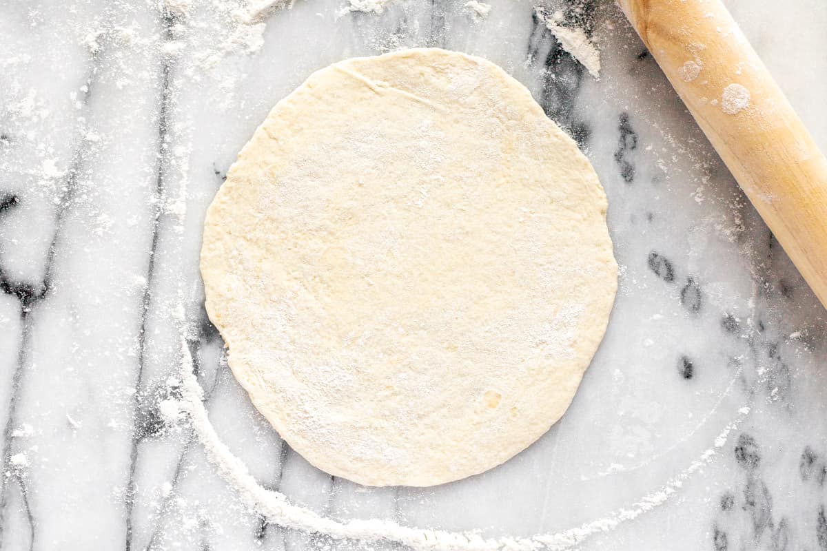 Chalupa dough rolled into a thin disk on a marble counter top. 
