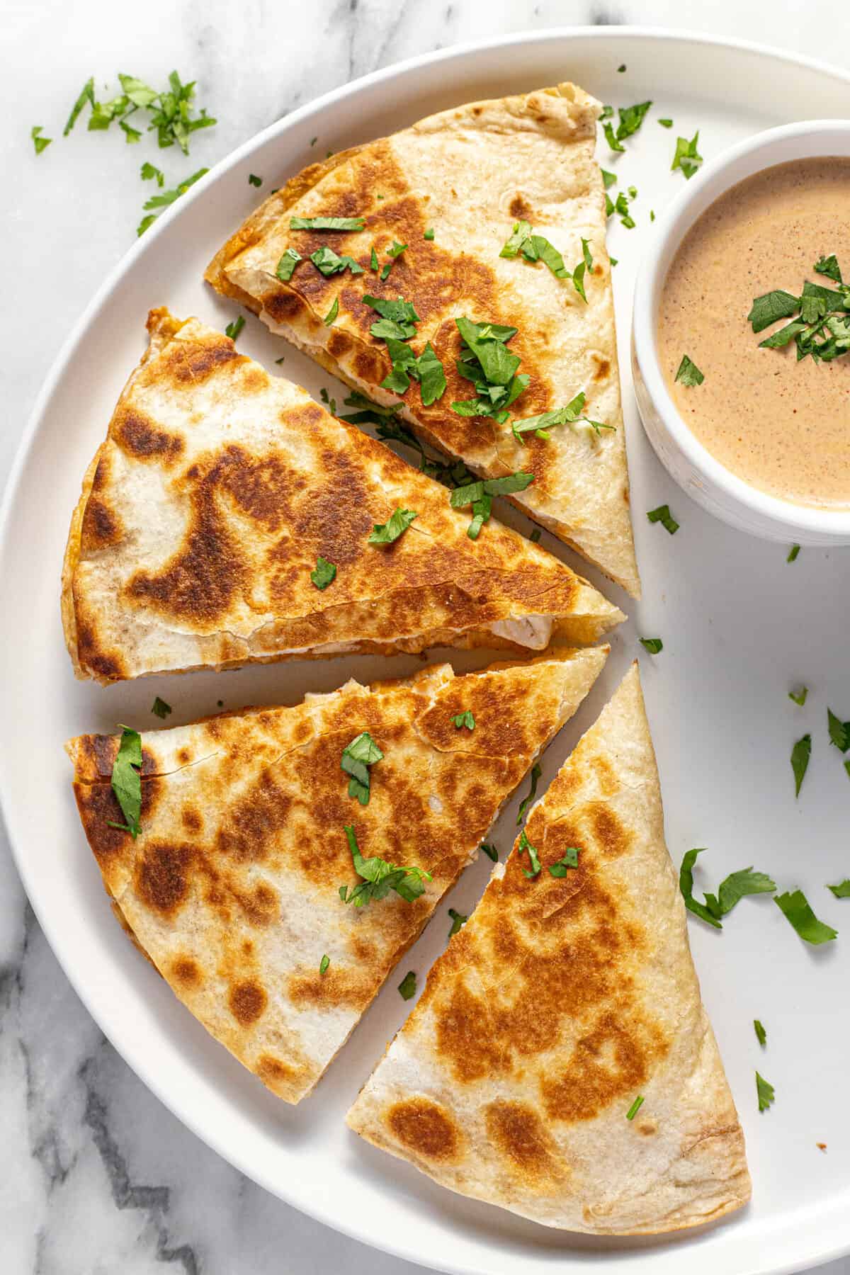 Copycat Taco Bell chicken quesadilla on  a white plate with a small bowl of quesasdilla sauce.
