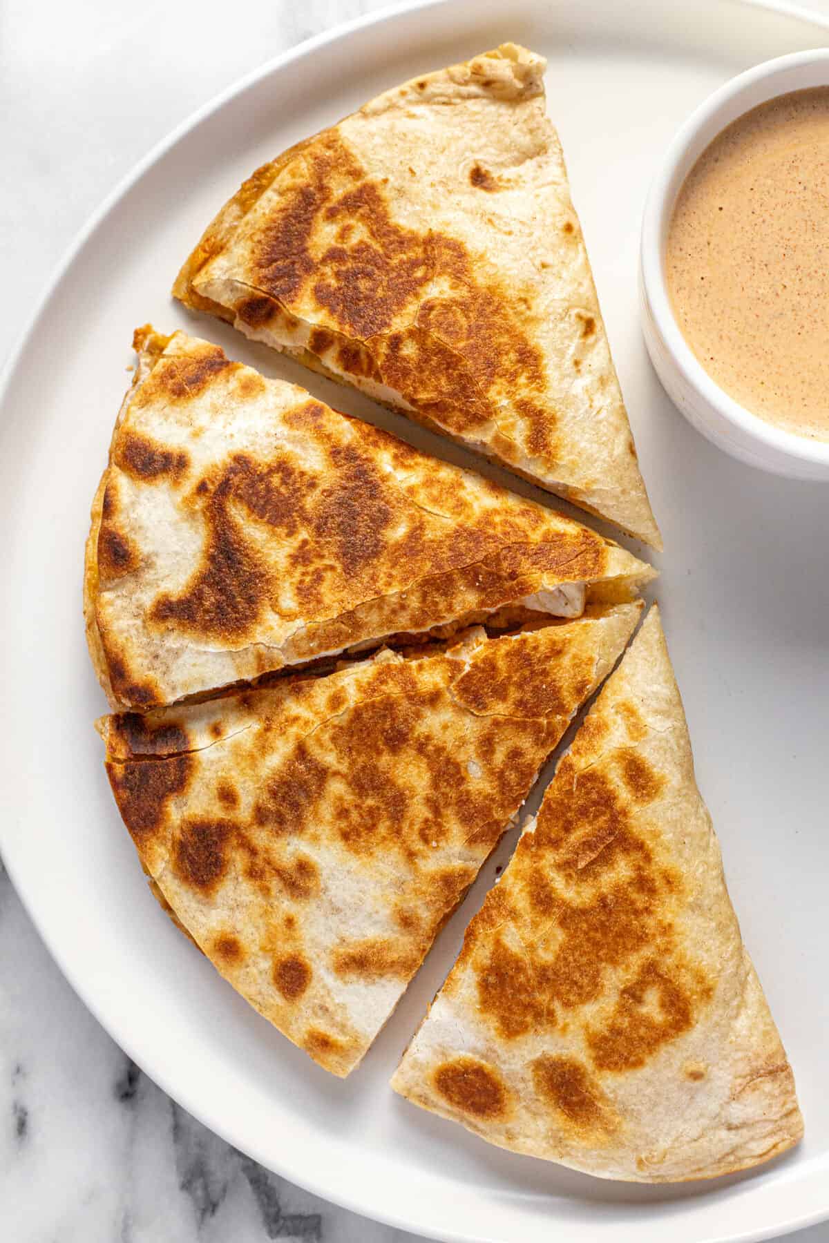 Copycat Taco Bell chicken quesadilla on  a white plate with a small bowl of quesasdilla sauce.