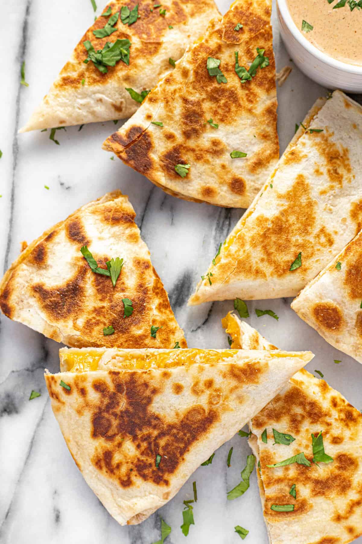 Triangles of chicken quesadilla on a white marble counter top garnished with fresh cilantro.
