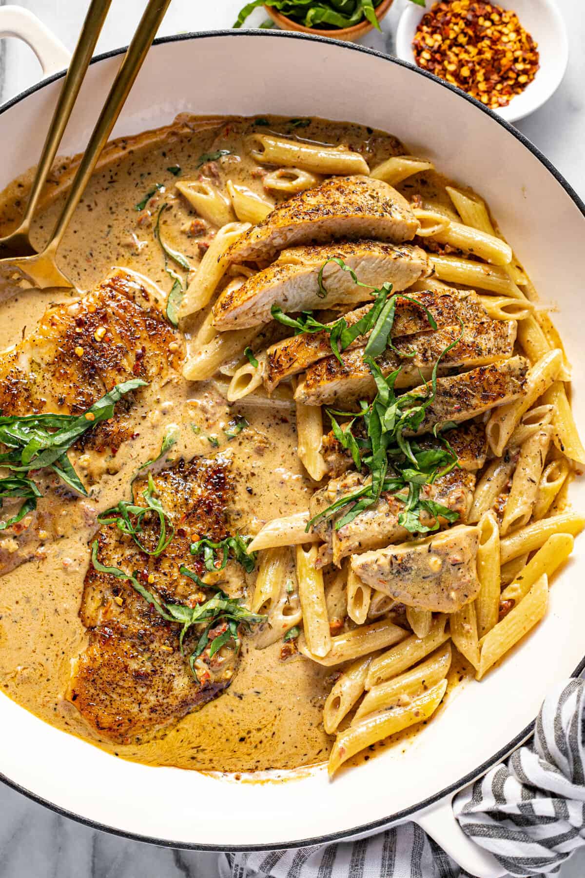 Large white pan filled with sauteed chicken, creamy garlic sauce, and pasta.