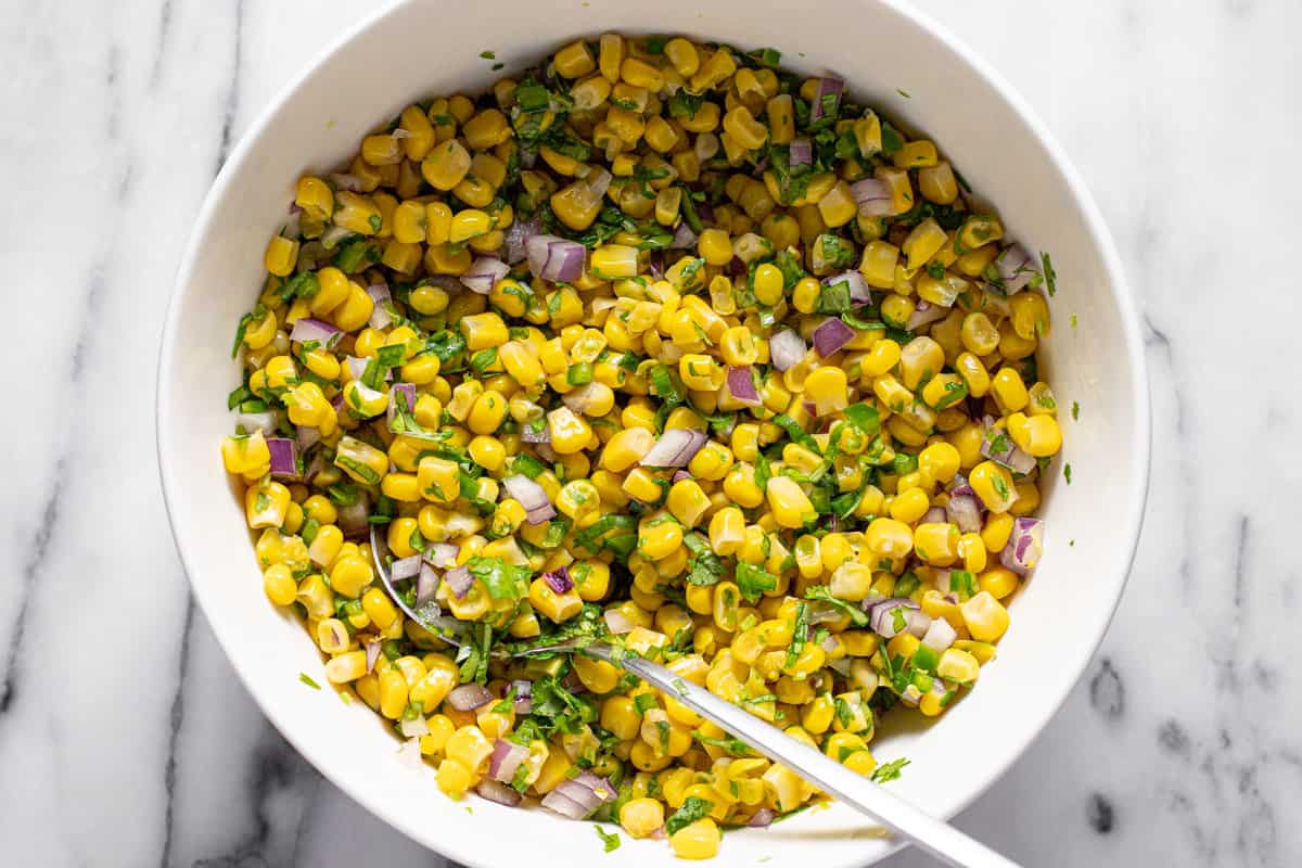 Freshly made corn salsa in a white bowl with a spoon.
