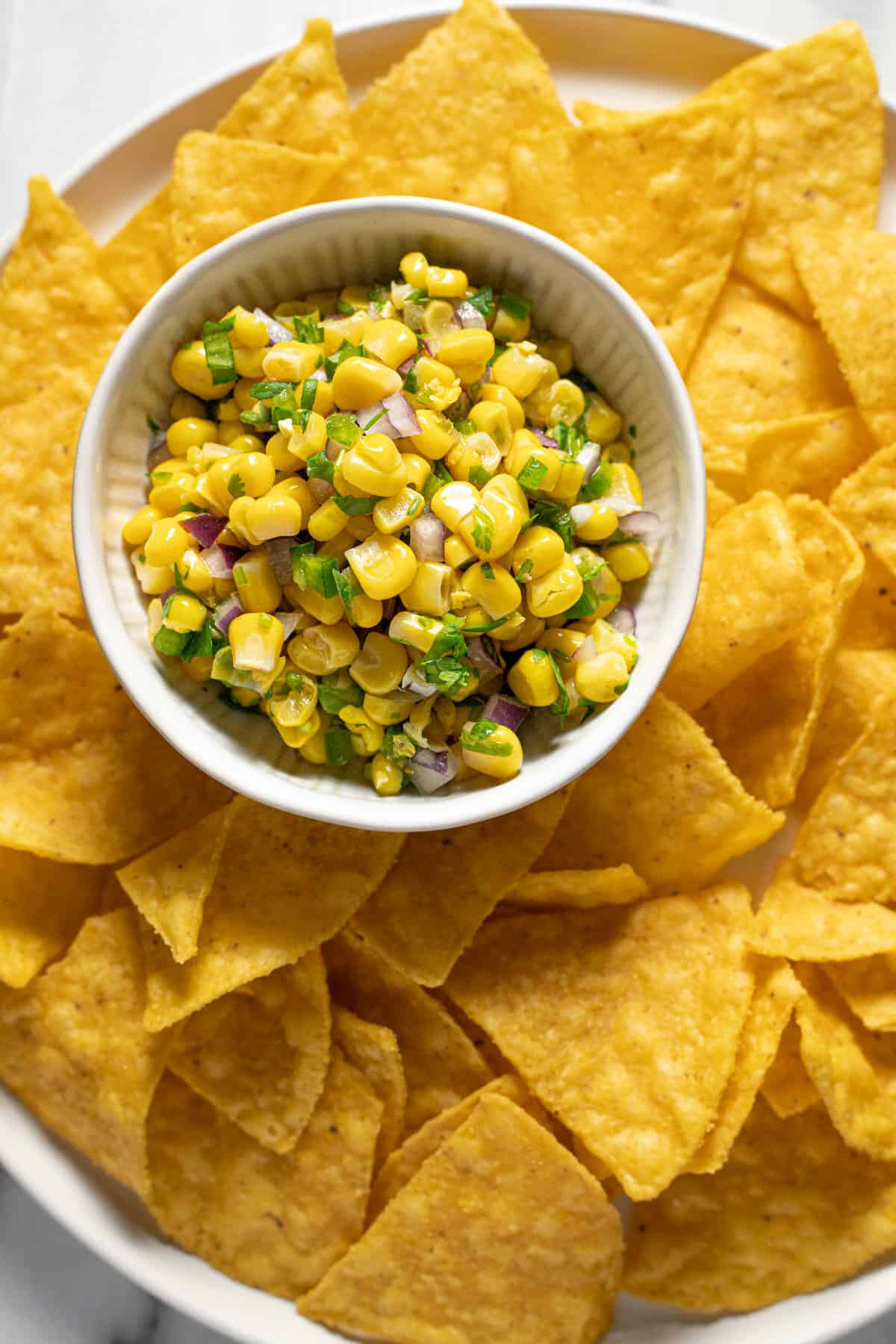 Small white bowl of corn salsa on a plate of tortilla chips.