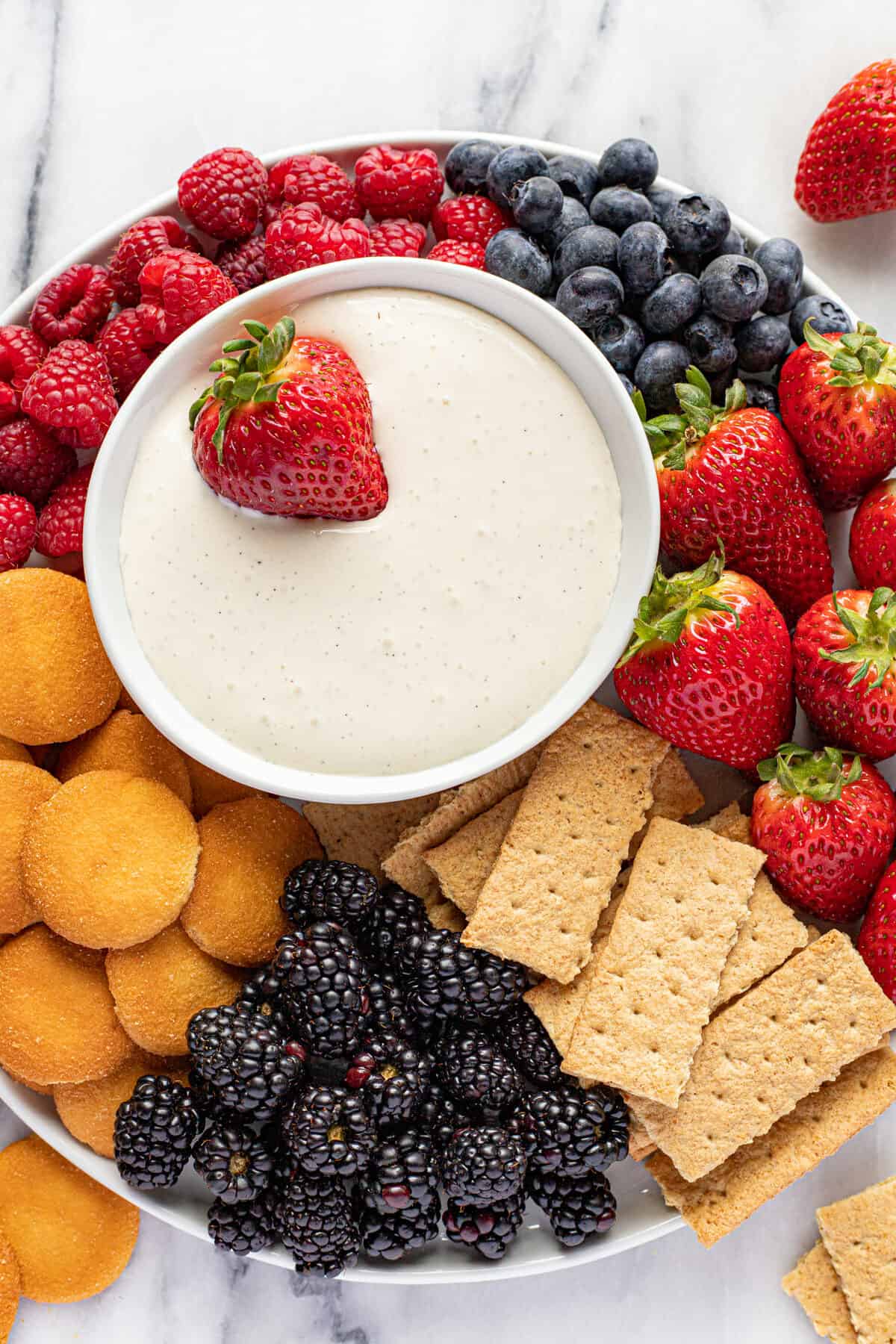 Platter of fruit, graham crackers, and Nilla wafers with a small bowl of fruit dip.
