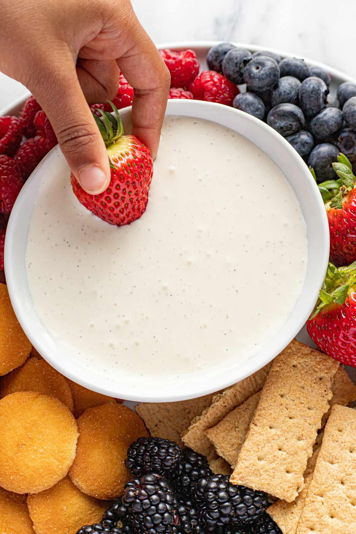 A small hand dipping a strawberry into a bowl of creamy fruit dip.