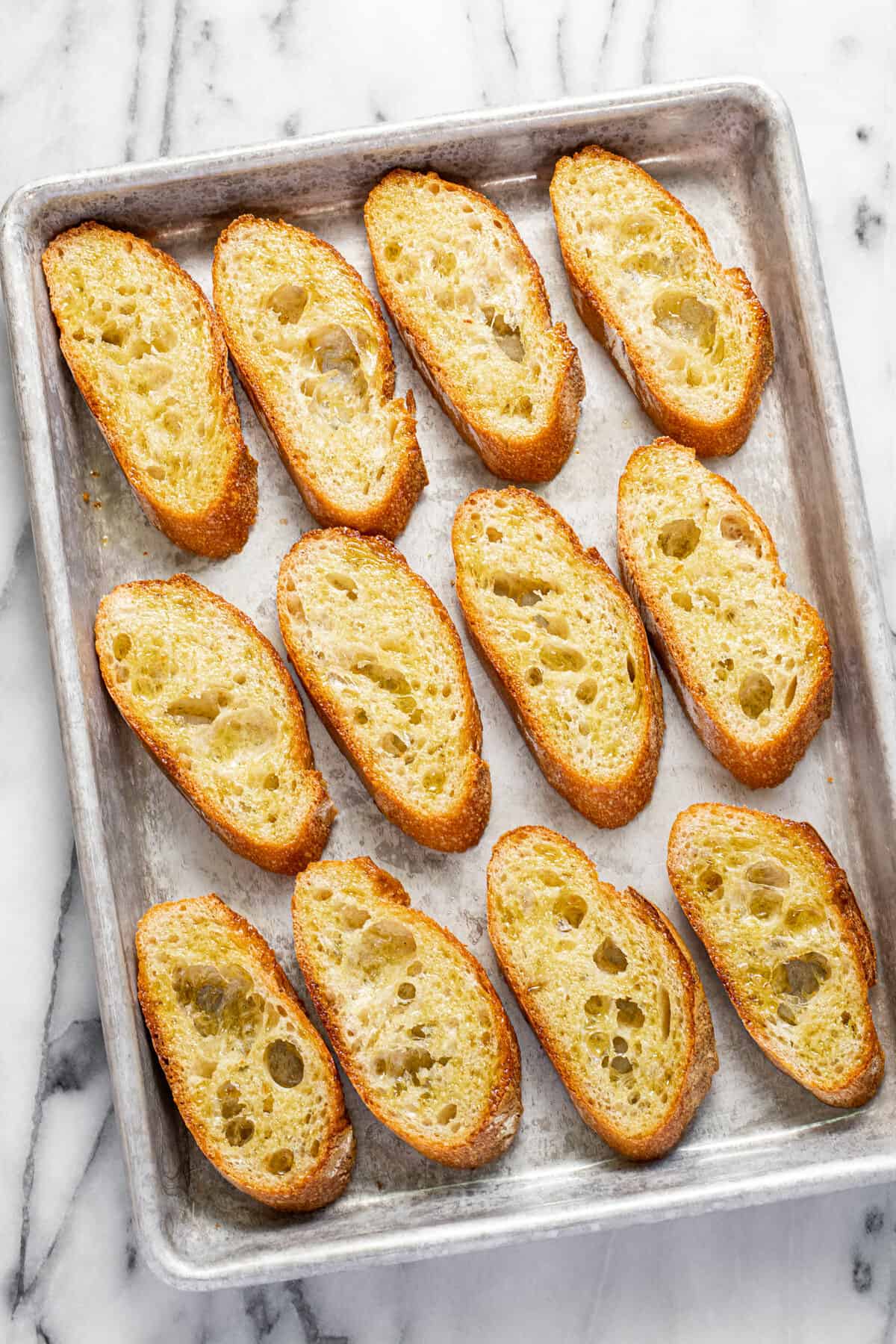 Sliced French bread brushed with olive oil on a baking sheet.