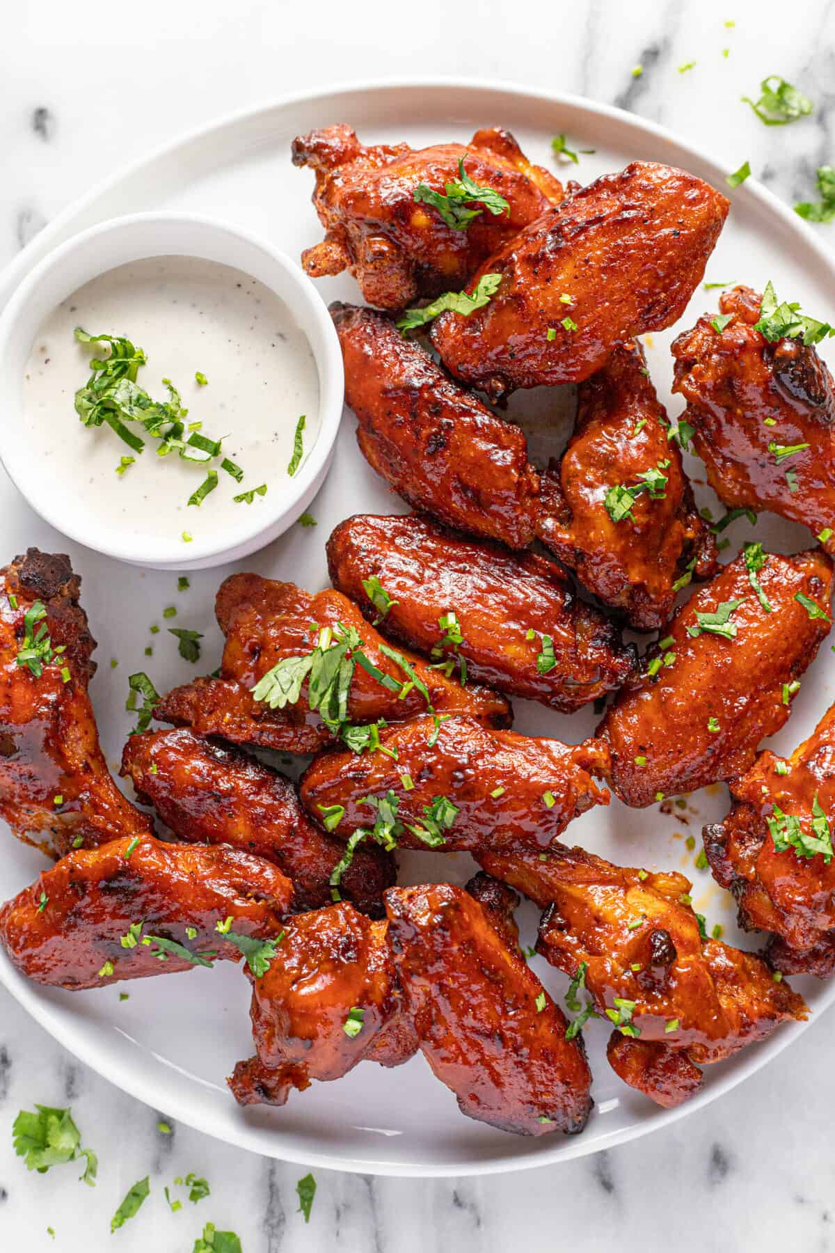 White plate filled with BBQ smoked chicken wings and a small bowl of ranch dressing.