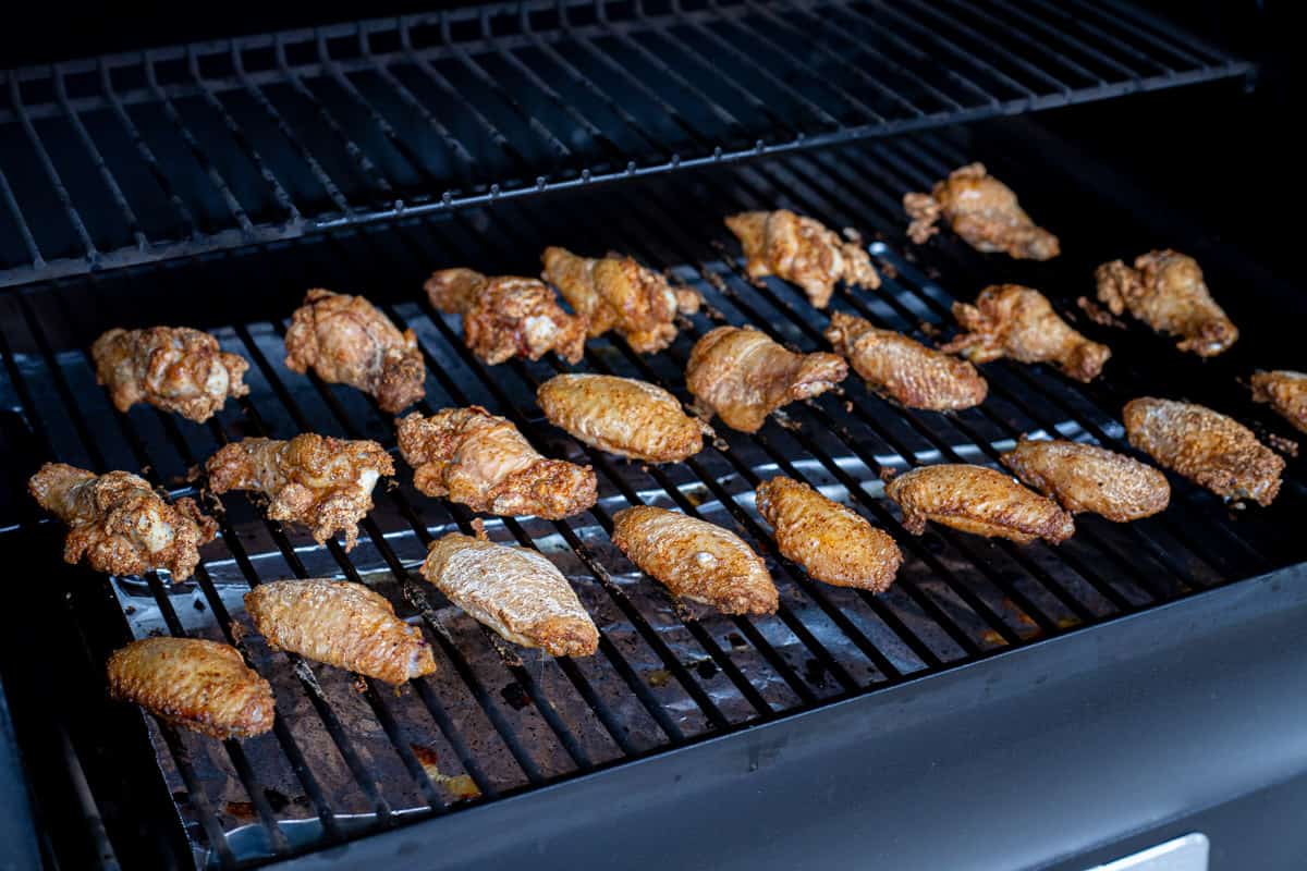 Grill grate with three rows of chicken wings smoking on the smoker.